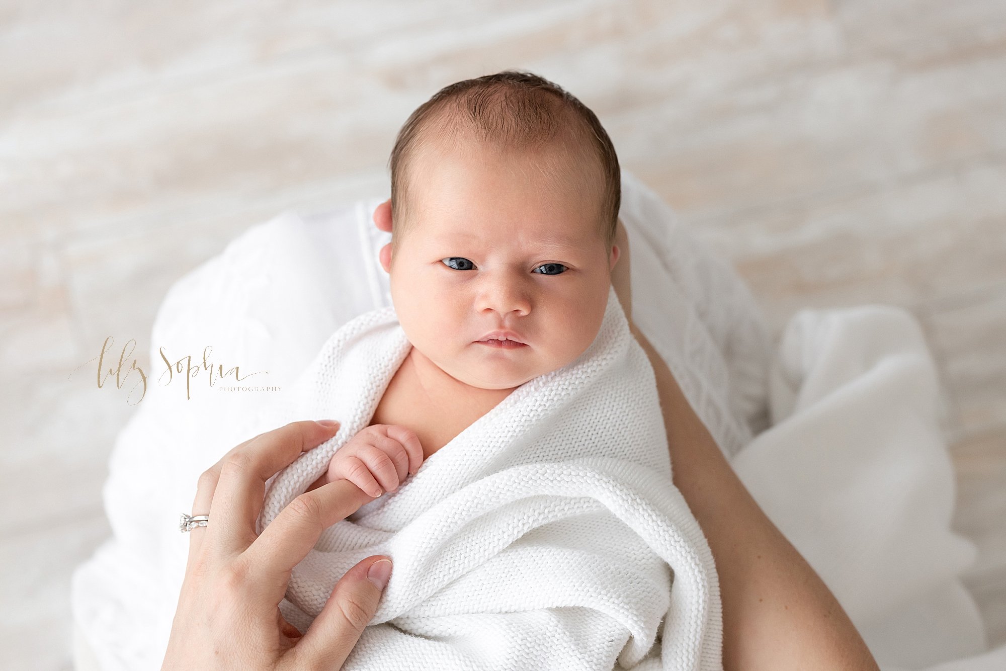  Newborn photo of a wide awake newborn baby girl with her head held in her mother’s right hand and her left index finger being clutched by her baby girl as she sits in a studio near Alpharetta in Atlanta that uses natural light. 