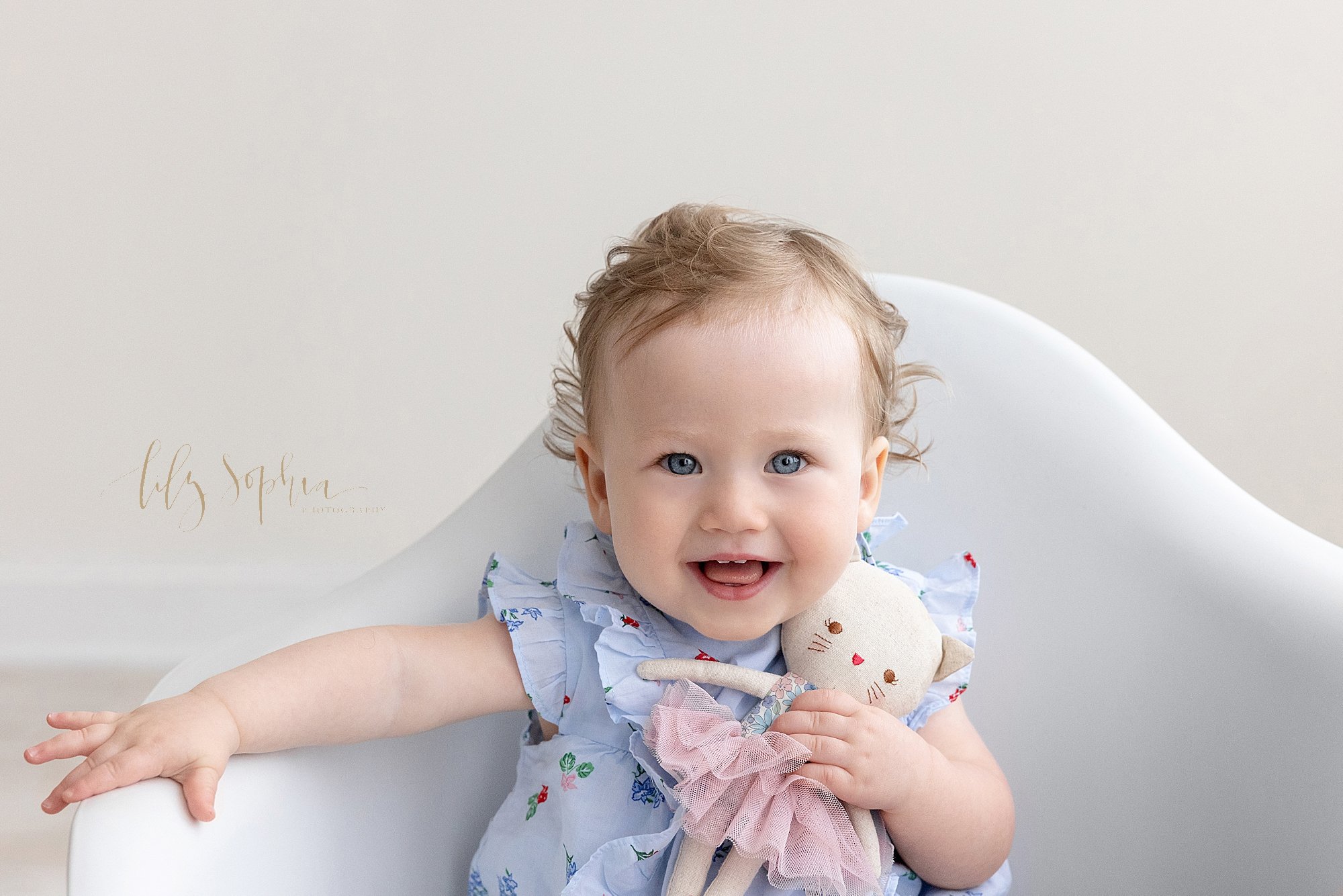  Baby photo of a baby girl as she sits in a white molded chair with her stuffed cat taken near Brookhaven in Atlanta in a natural light photography studio. 