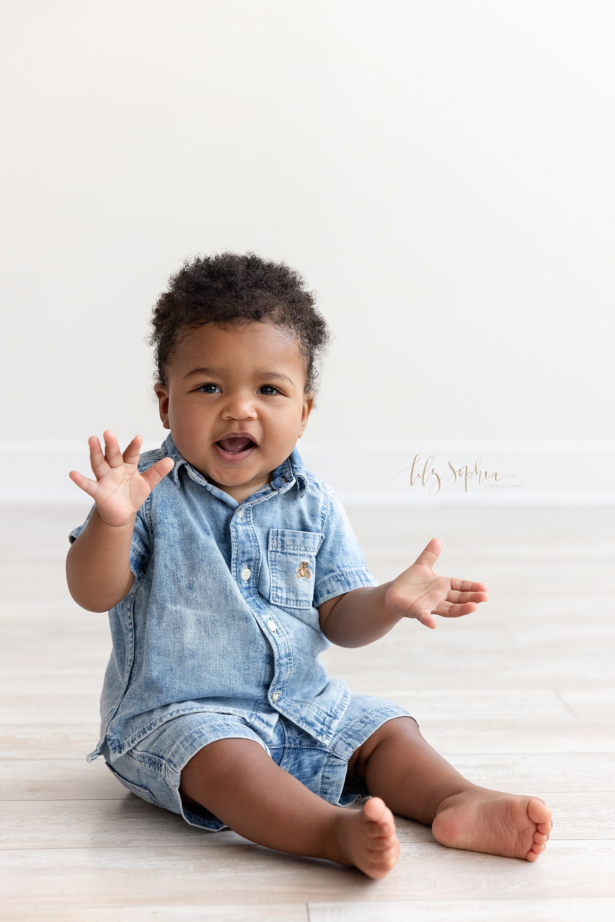  Baby portrait of a nine month old African-American baby boy as he sits on the floor of a natural light studio and claps his hands taken near Poncey Highlands in Atlanta, Georgia. 