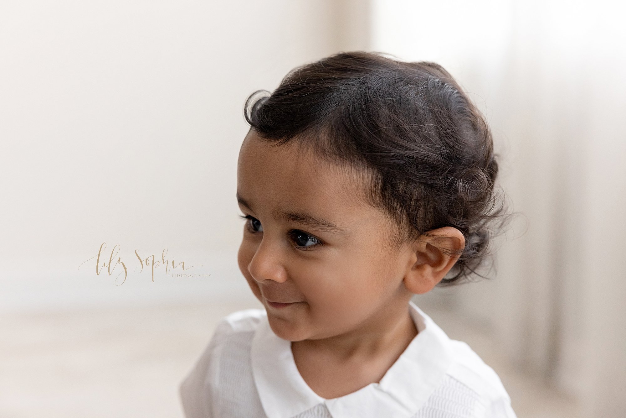  Close-up picture of a black curly haired Indian baby  boy as he stands next to a window streaming natural light in a photography studio near Decatur in Atlanta, Georgia. 