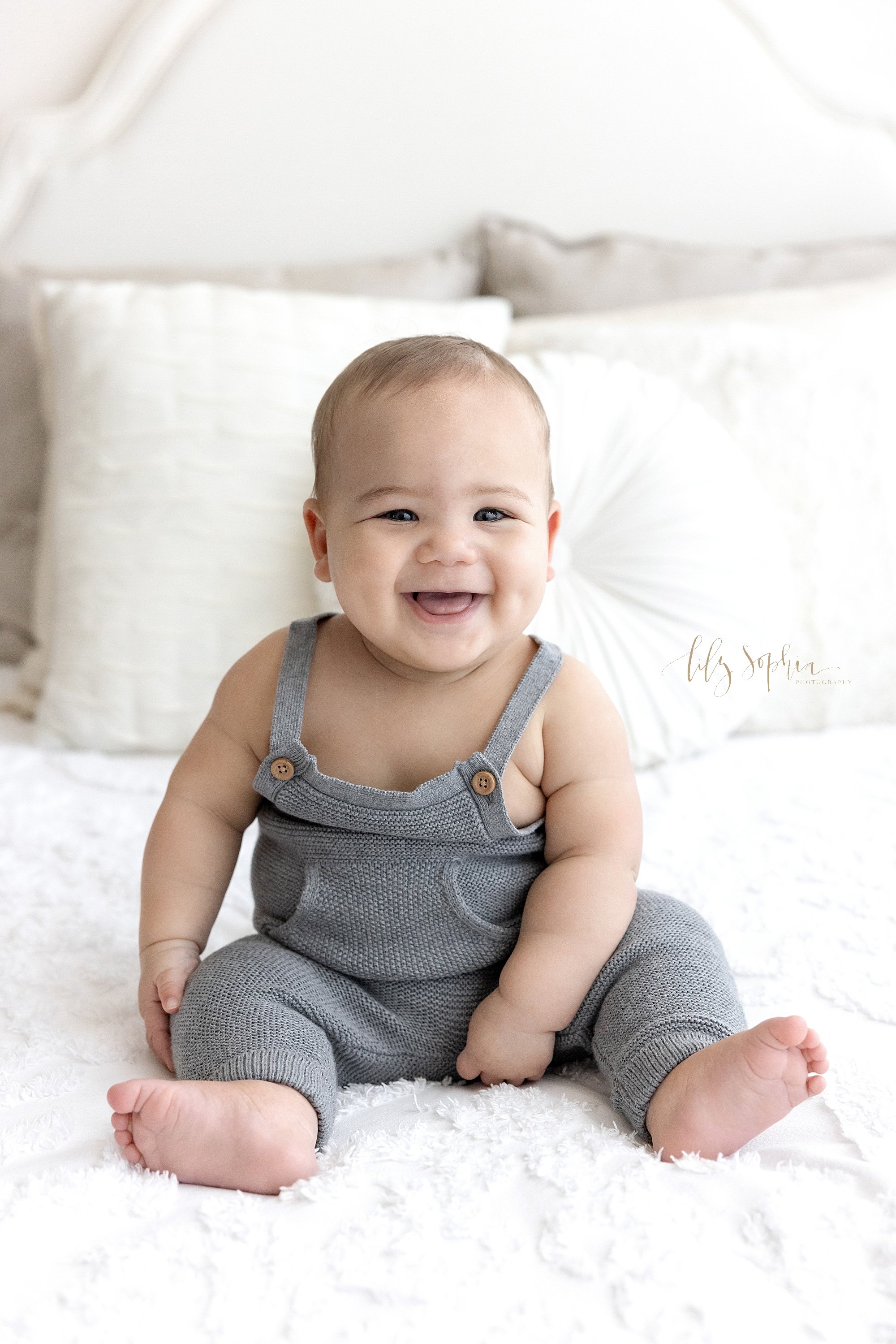  Milestone photo of a baby boy as he smiles and sits on top of a bed taken in a studio in Ponce City Market in Atlanta, Georgia that uses natural light. 