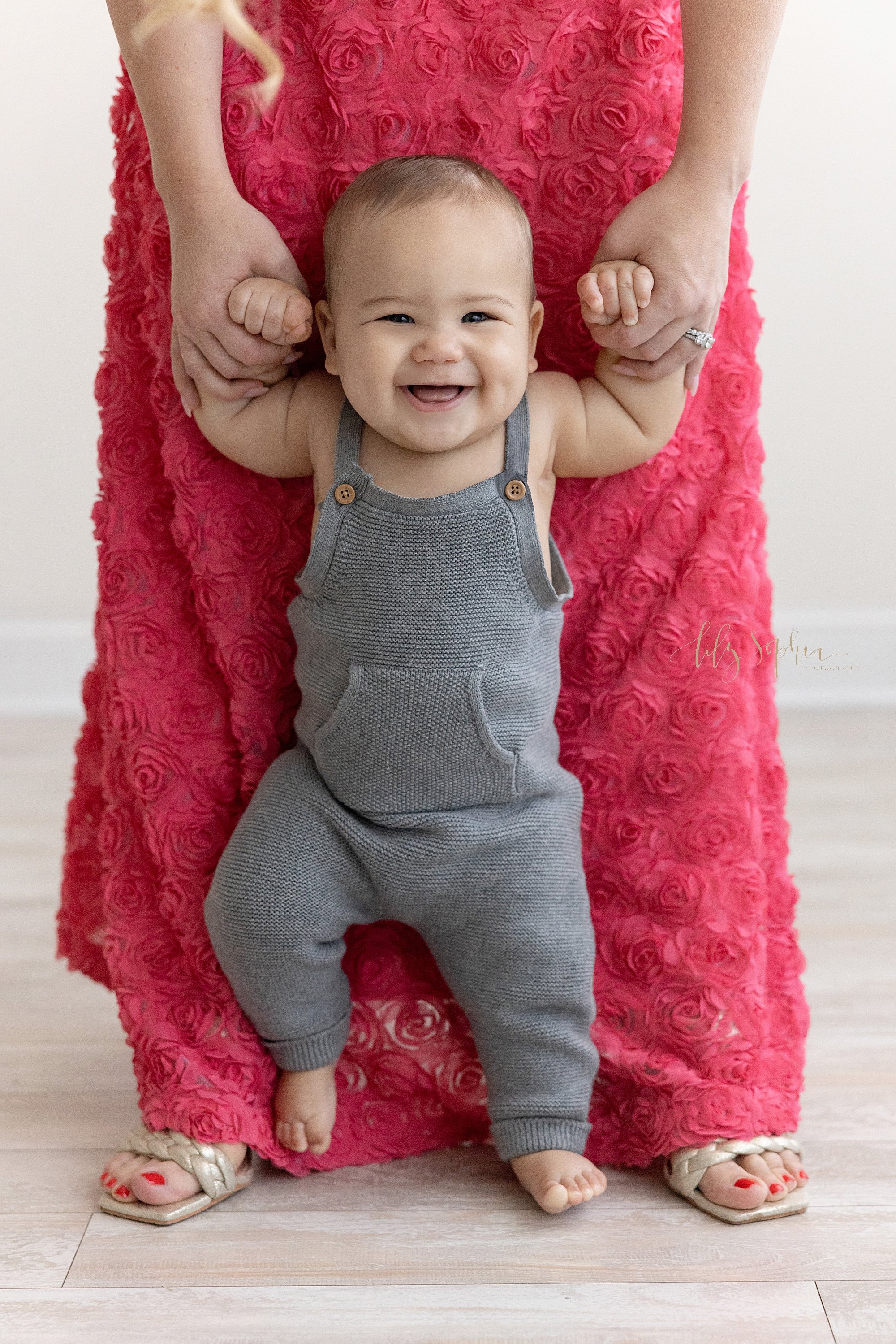  Baby picture of  a proud and happy baby boy as his arms are held by his mother, so he can walk in front of her taken near Oakhurst in Atlanta, Georgia in a natural light studio. 