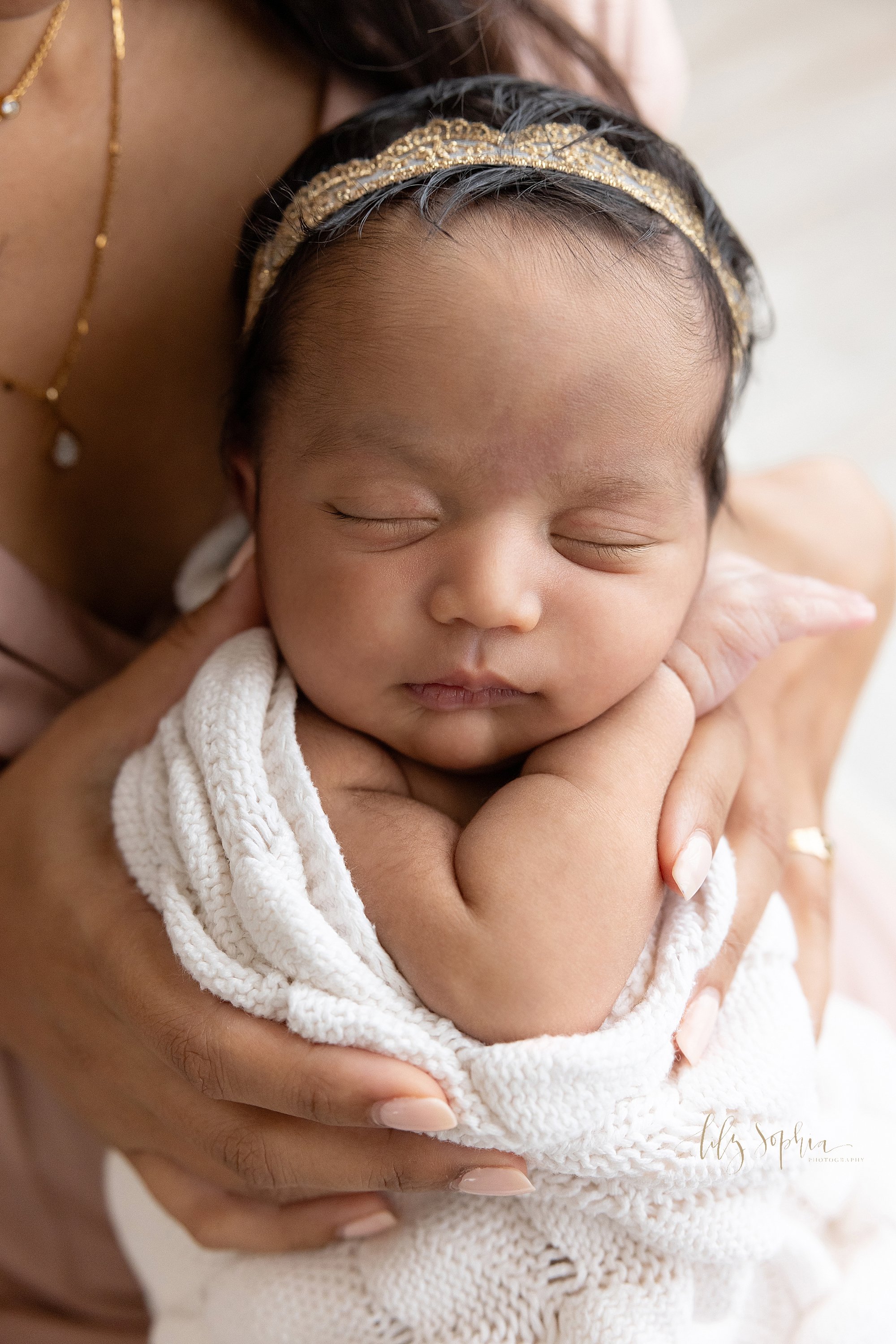  Close-up newborn portrait of a peacefully sleeping baby girl as she is held in her arms by her mother and she rests her head on her right arm taken near Smyrna in Atlanta in a natural light studio. 