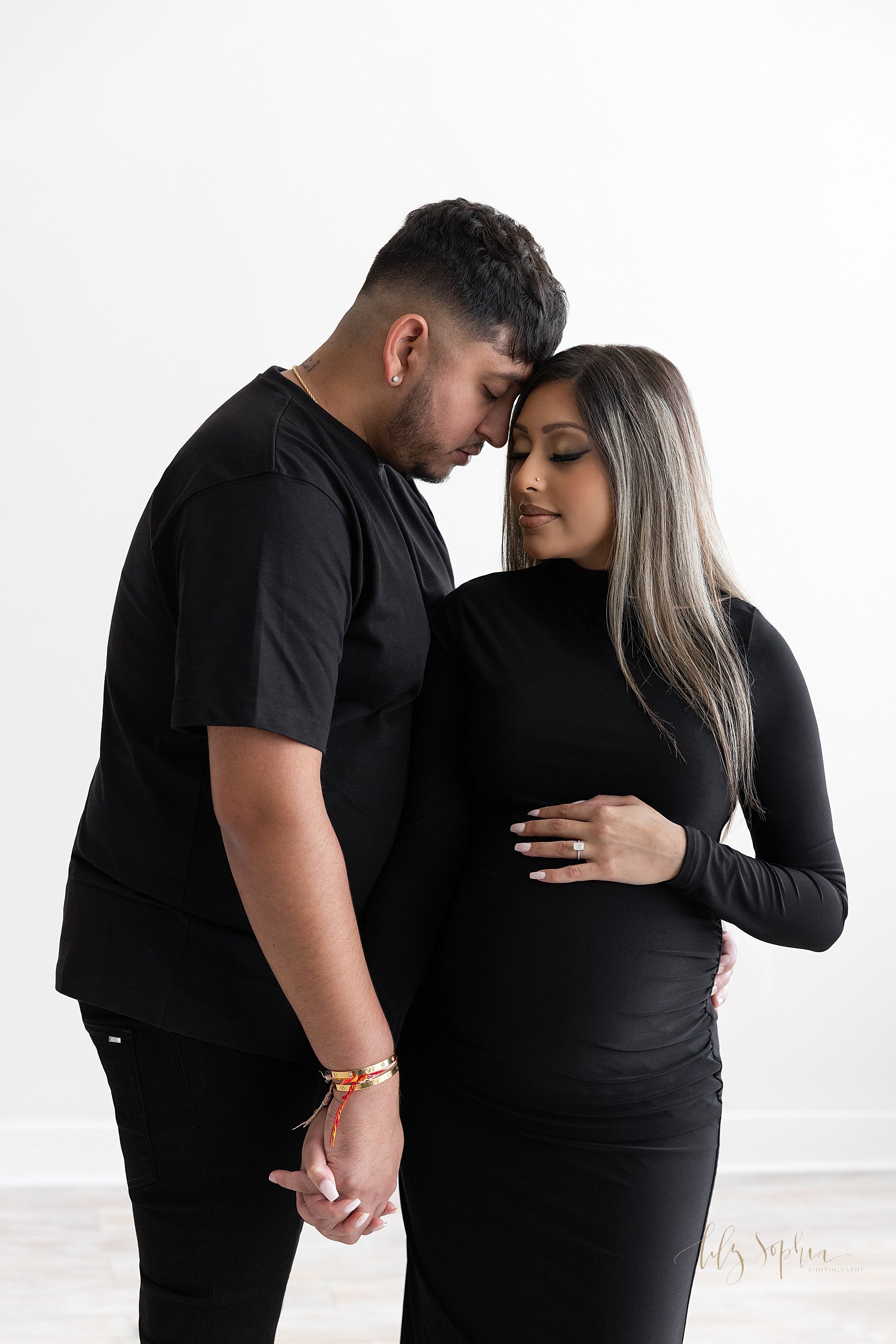 Maternity portrait of a pregnant mother standing with her left hand on top of her belly as her husband stands to her right side and he holds her right hand with his right hand and he places his forehead on her head taken near Oakhurst in Atlanta in 