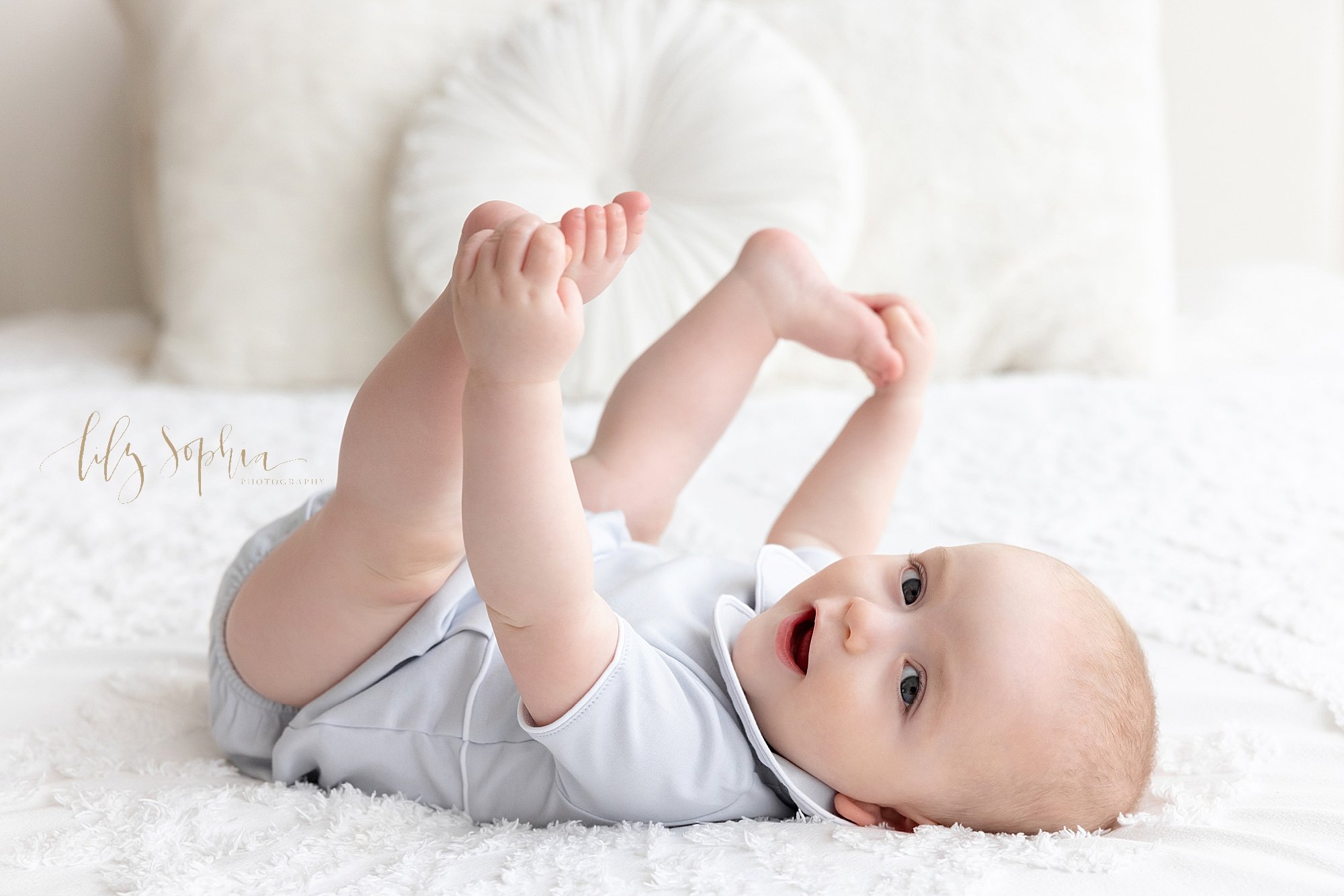  Milestone baby photo of baby boy lying on his back on a bed as he holds his feet in his hands taken in a natural light photography studio near Midtown in Atlanta, Georgia. 