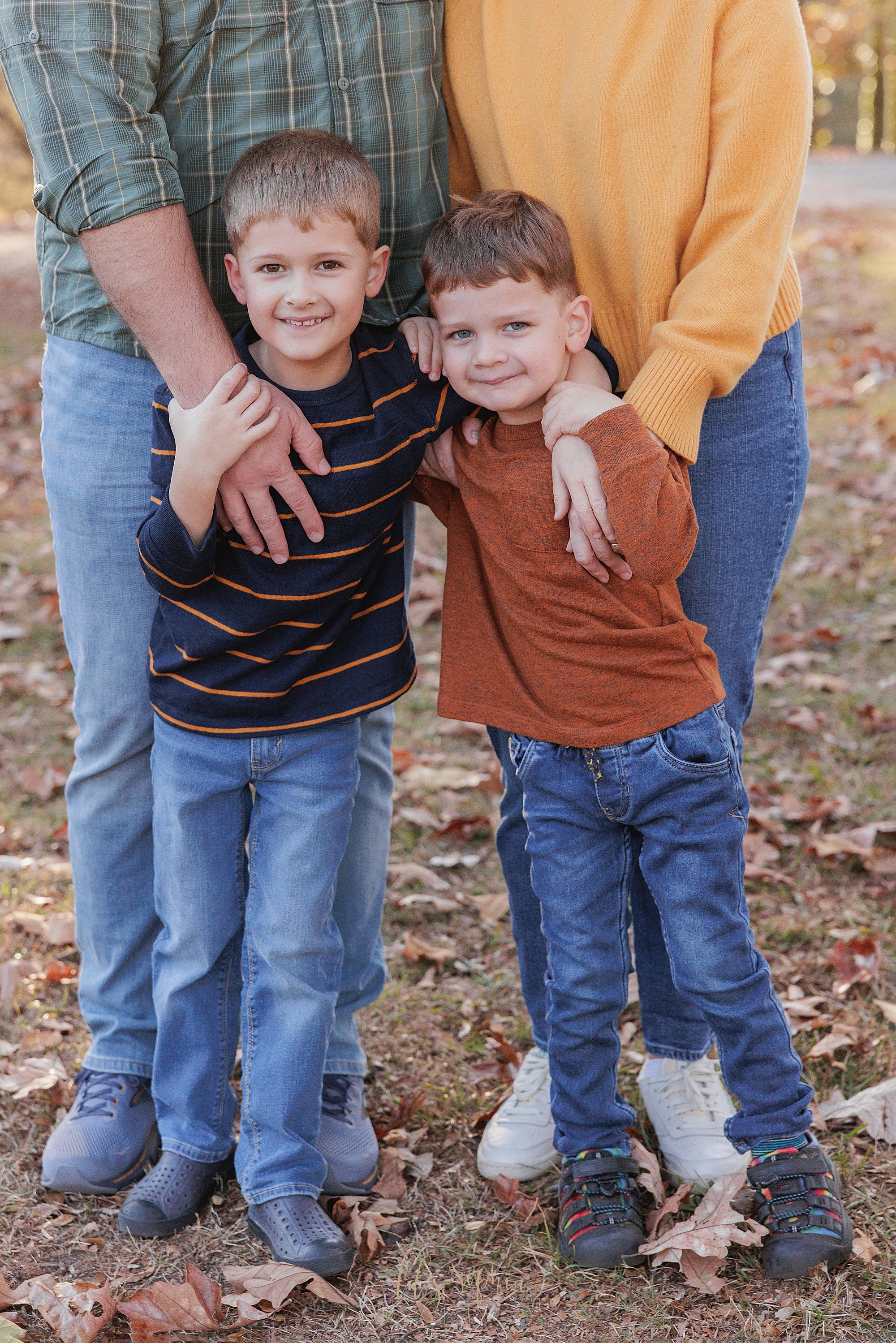  Family photo of brothers with their arms wrapped around each other’s shoulders as they stand in front of their parents during autumn in a park near Atlanta, Georgia. 