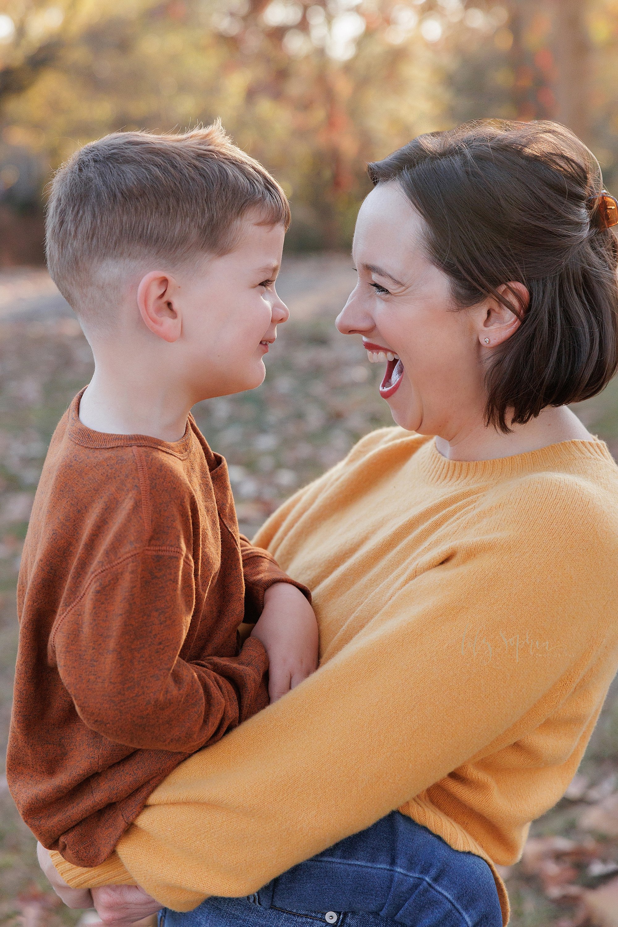  Close-up family portrait of a mother holding her young son as they talk and laugh together in an Atlanta park at sunset. 