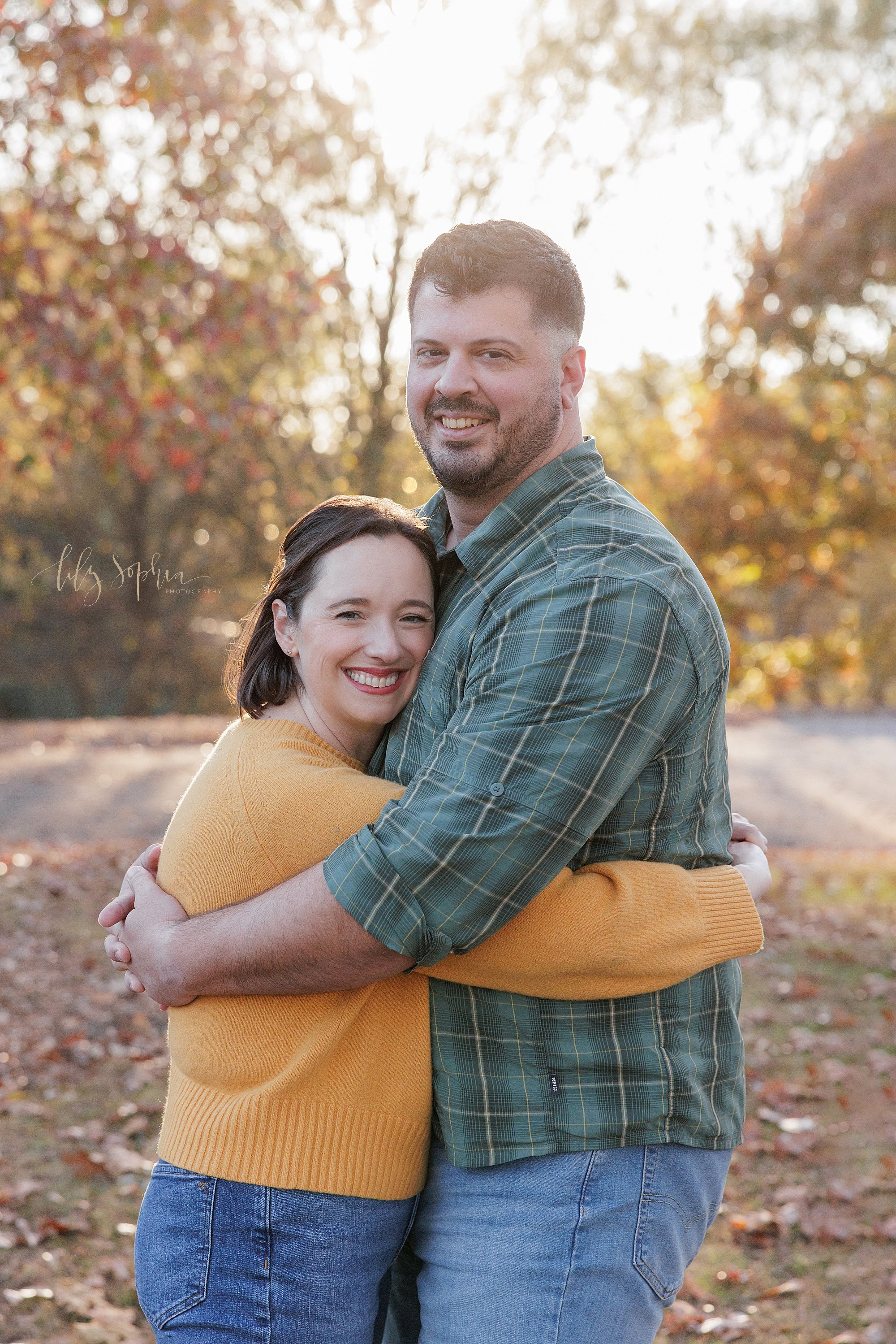  Family picture of a husband a wife as they stand and hug one another taken at sunset near Atlanta, Georgia in a park during autumn. 