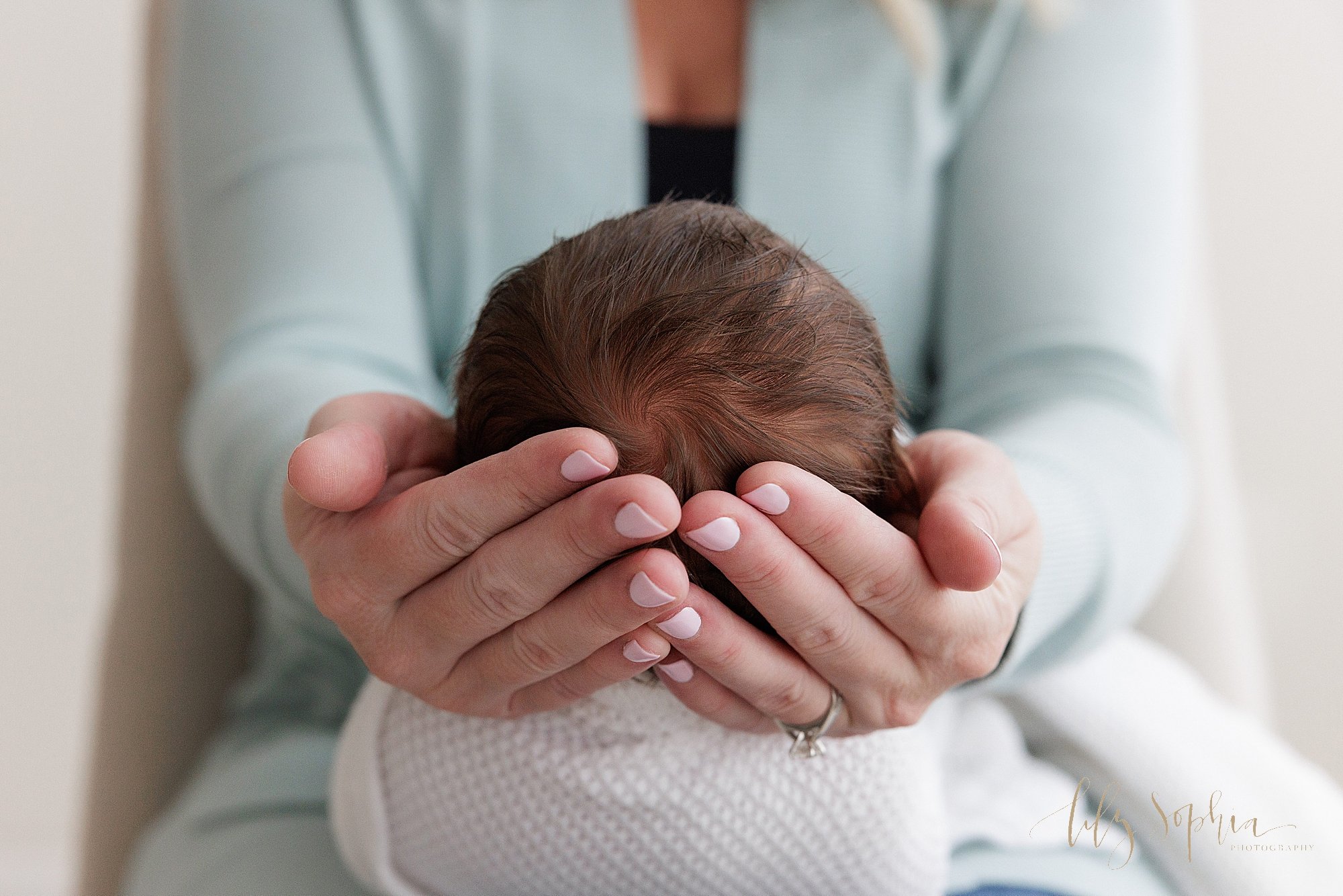 Close-up newborn photo of a mother holding her newborn son’s head in the palms of her hand taken near Virginia Highlands in Atlanta in a natural light studio. 