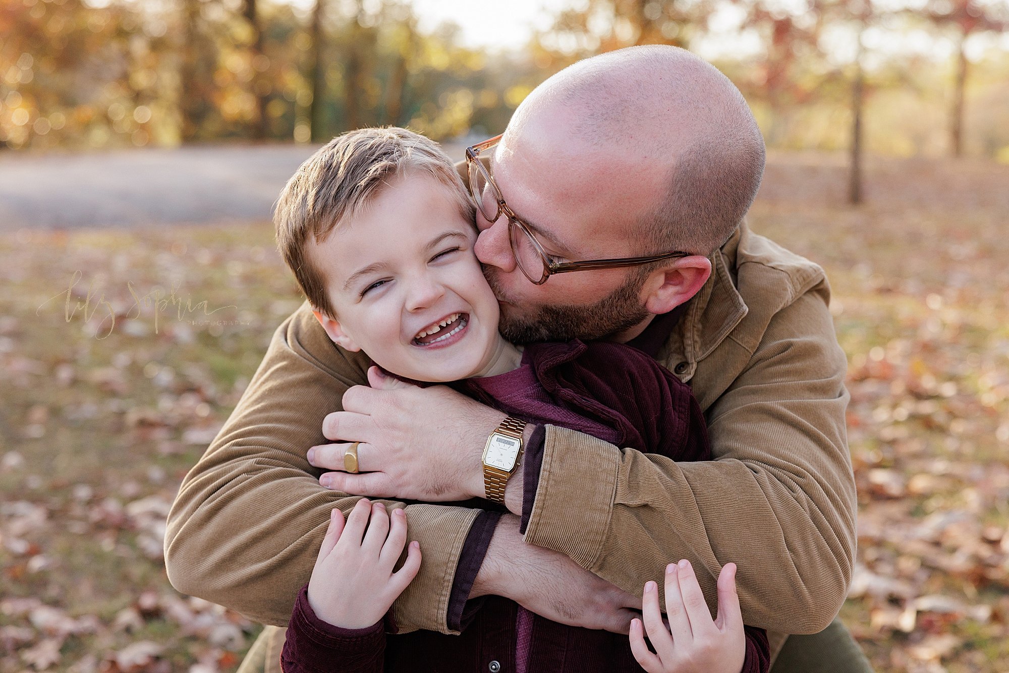  Father and son picture of a father wrapping his arms around his young son and kissing him on his cheek taken in a park near Atlanta at sunset during autumn. 