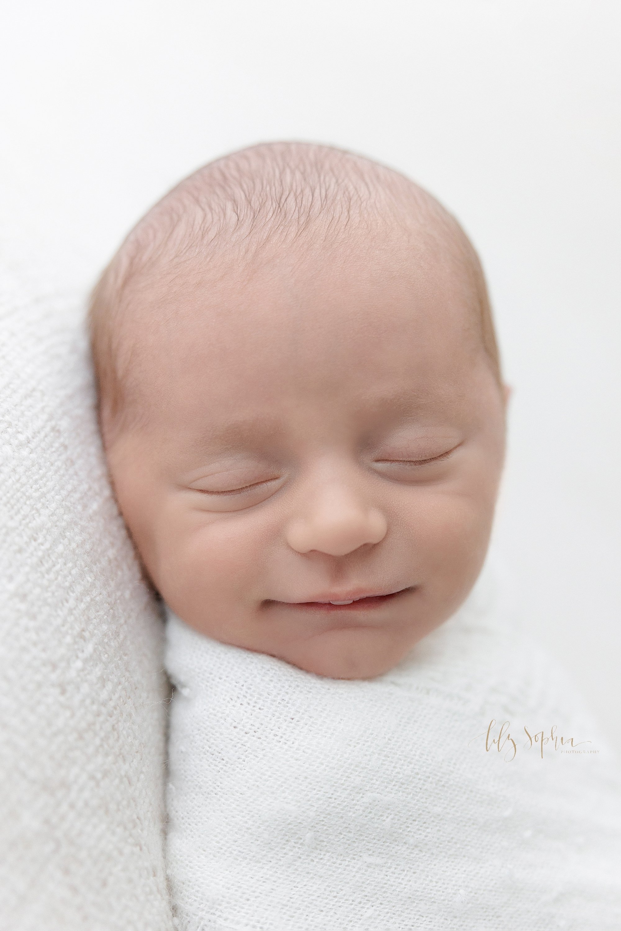  Newborn portrait of a peacefully sleeping newborn baby boy swaddled to his chin in a soft white blanket taken near Buckhead in Atlanta, Georgia in a natural light studio. 