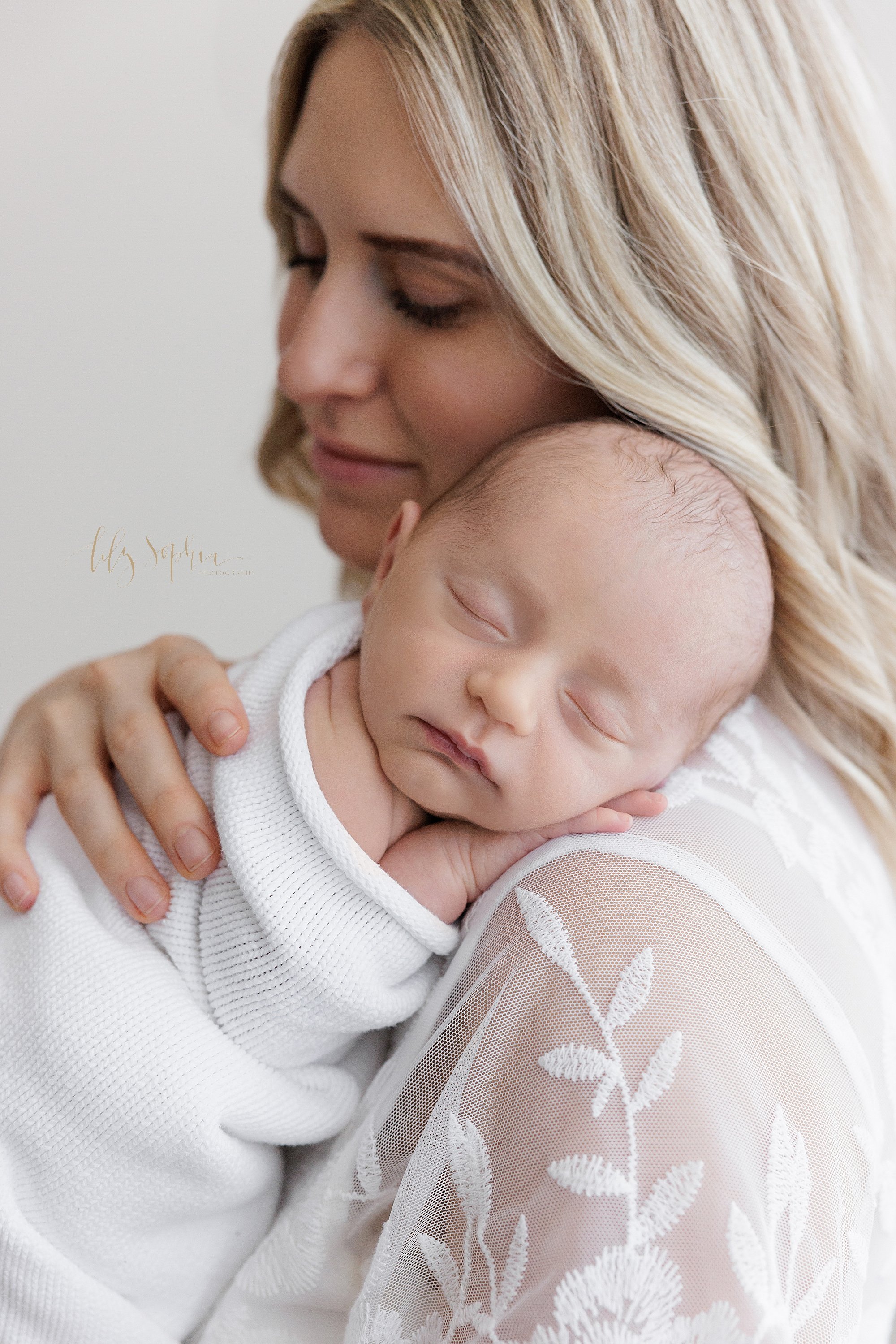  Close-up newborn portrait of a newborn baby boy taken in a natural light photography studio as he is being held by his mother and rests his head on her shoulder near Alpharetta in Atlanta. 