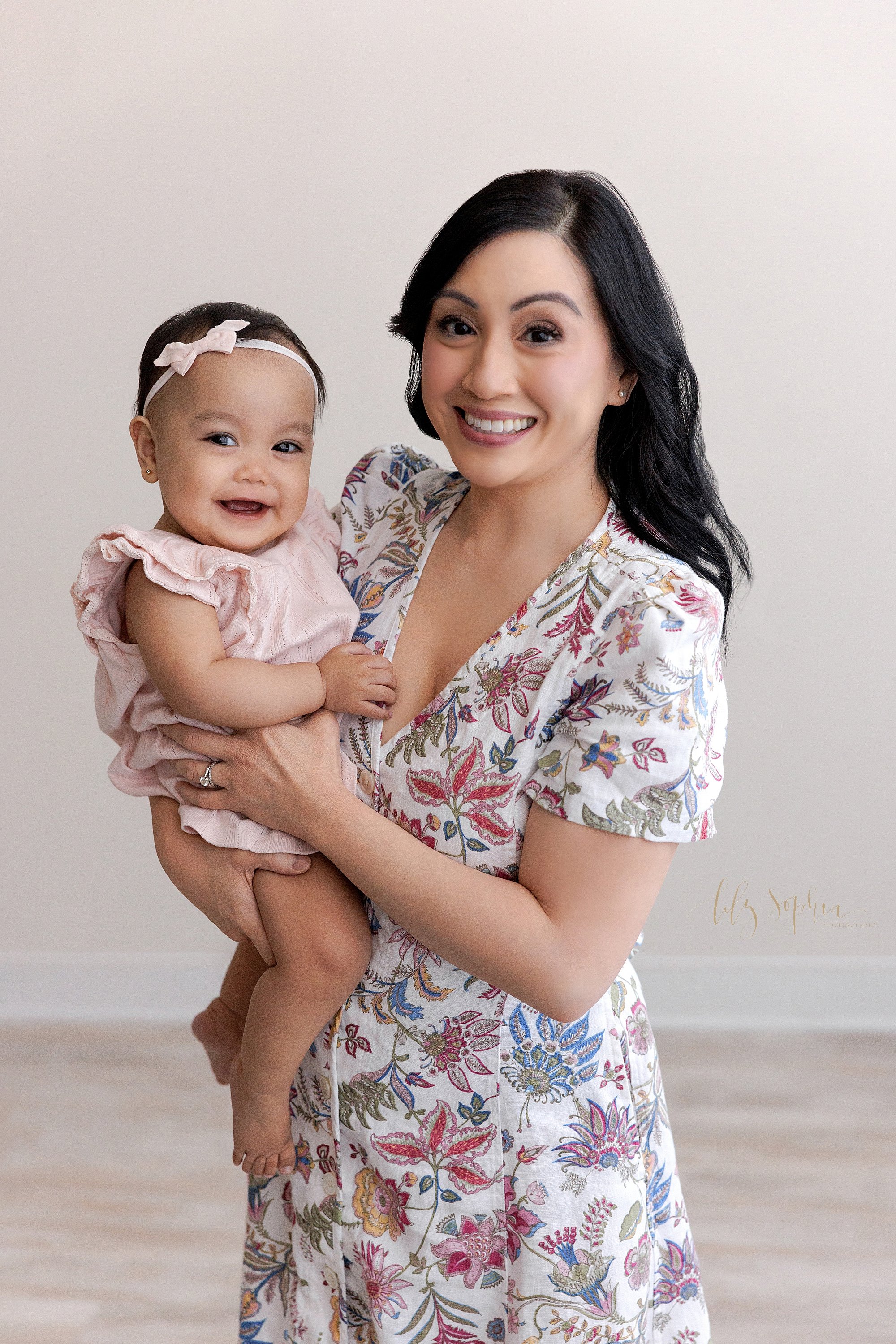  First birthday mother and daughter portrait of an Asian mother holding her smiling one year old daughter in her arms as she stands in a natural light studio near Old Fourth Ward in Atlanta. 