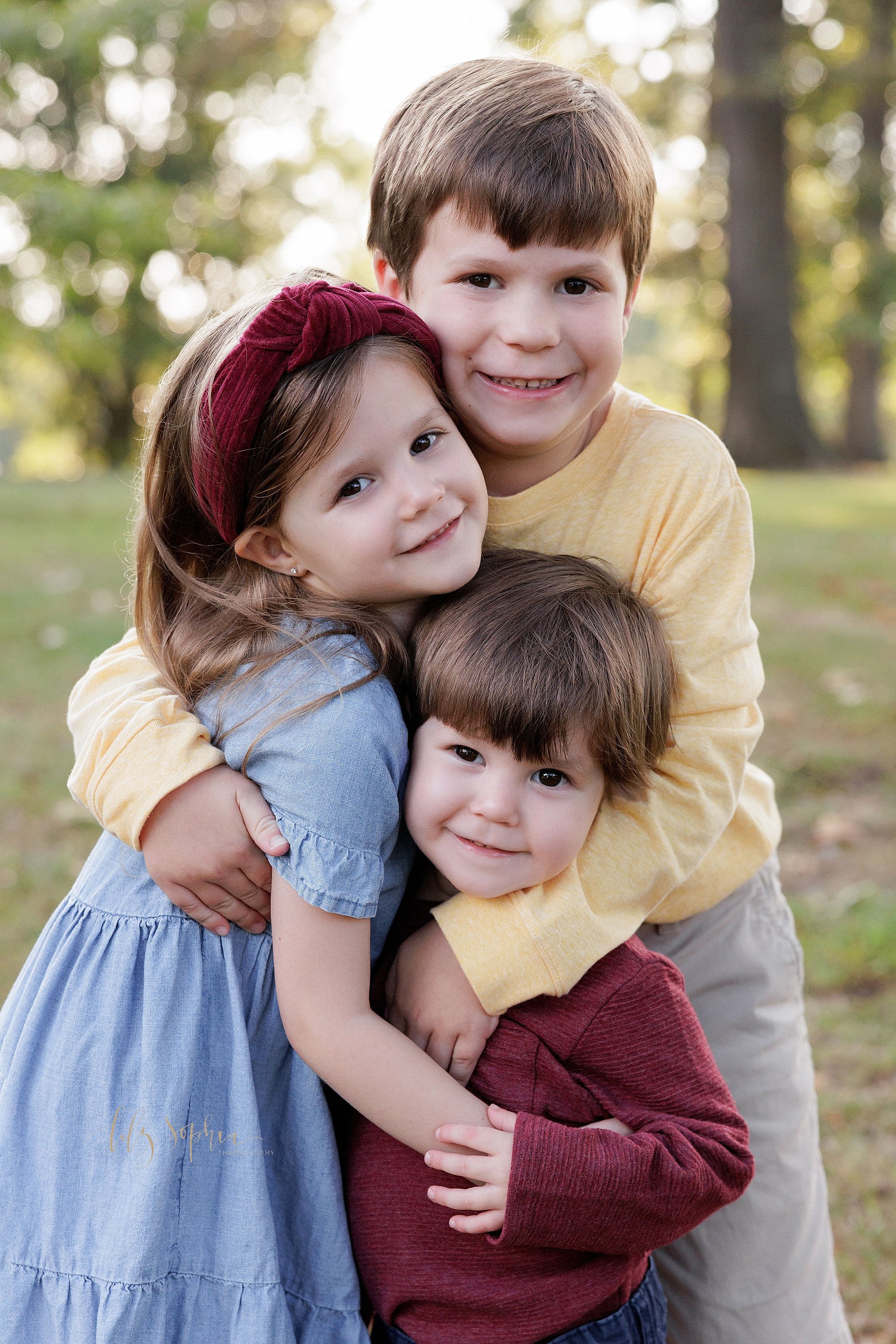  Sibling group hug is captured in a park near Atlanta, Georgia for a family photography session at sunset during the spring season. 