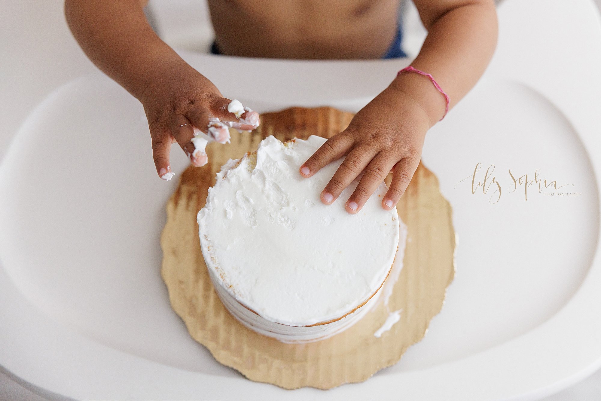  Close-up picture of the hands of a one year old boy as he digs into his smash cake while celebrating his first birthday taken in a natural light studio near Cumming in Atlanta, Georgia. 
