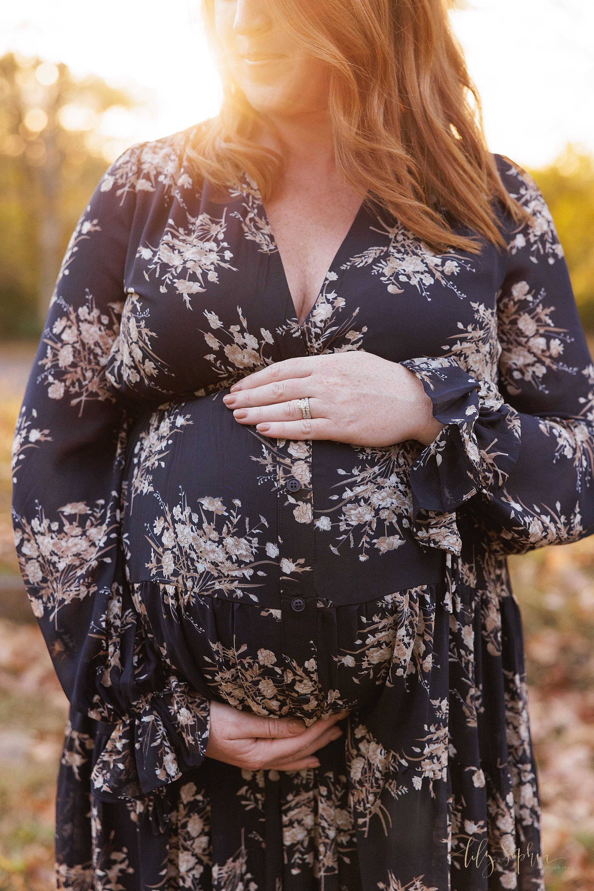  Close-up photo of the belly of an expectant mother framed with her hands for a maternity photo shoot at sunset during autumn in an Atlanta park. 
