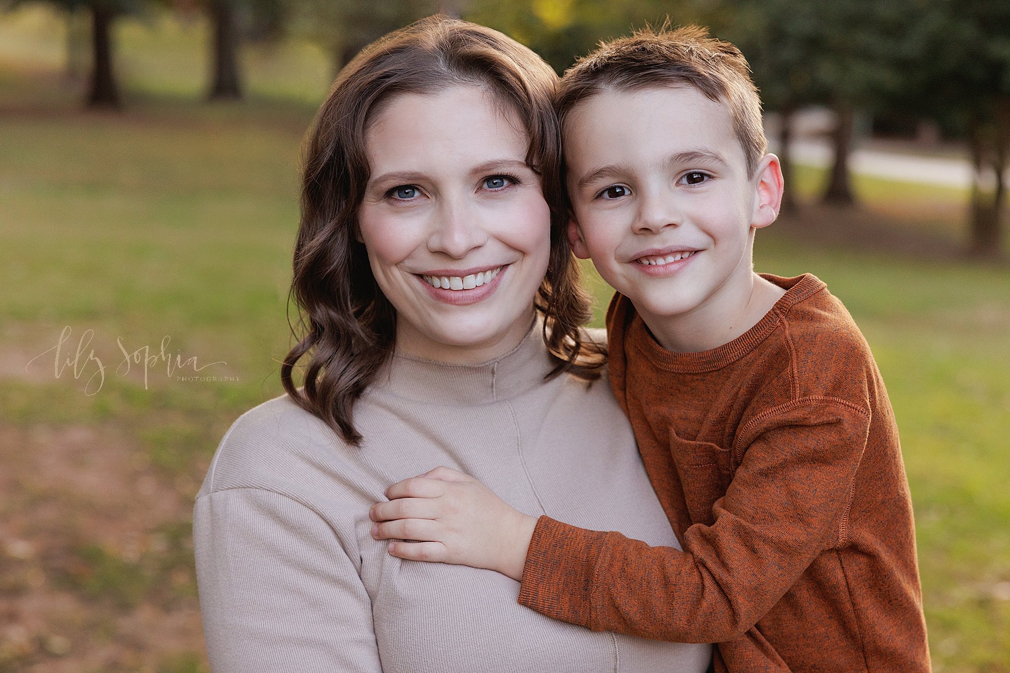  Family photo session with a mother holding her son at sunset as they stand in a park during autumn in Atlanta. 