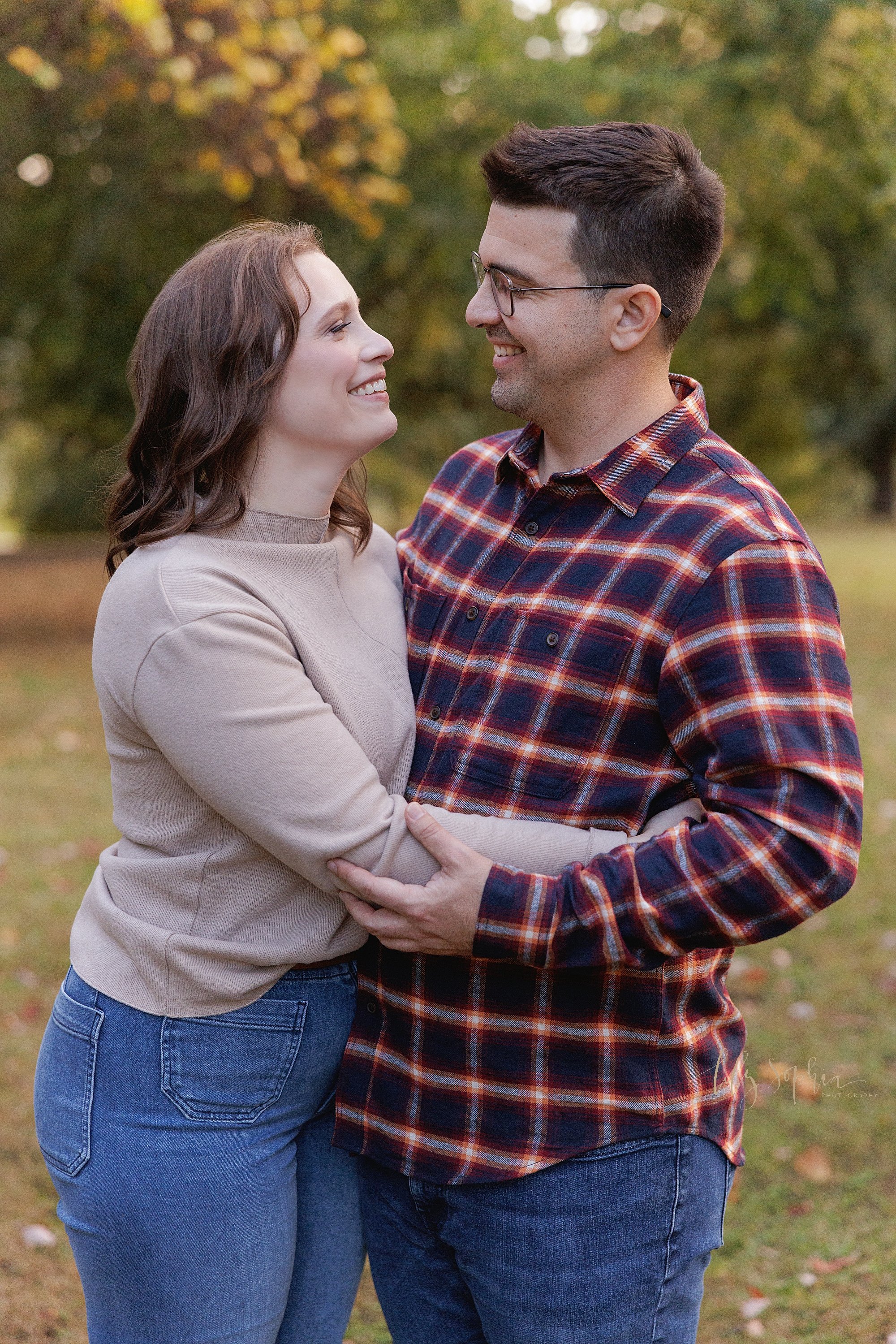  A husband and wife embrace each other while looking lovingly into each other’s eyes as they stand in an Atlanta park at sunset during autumn. 