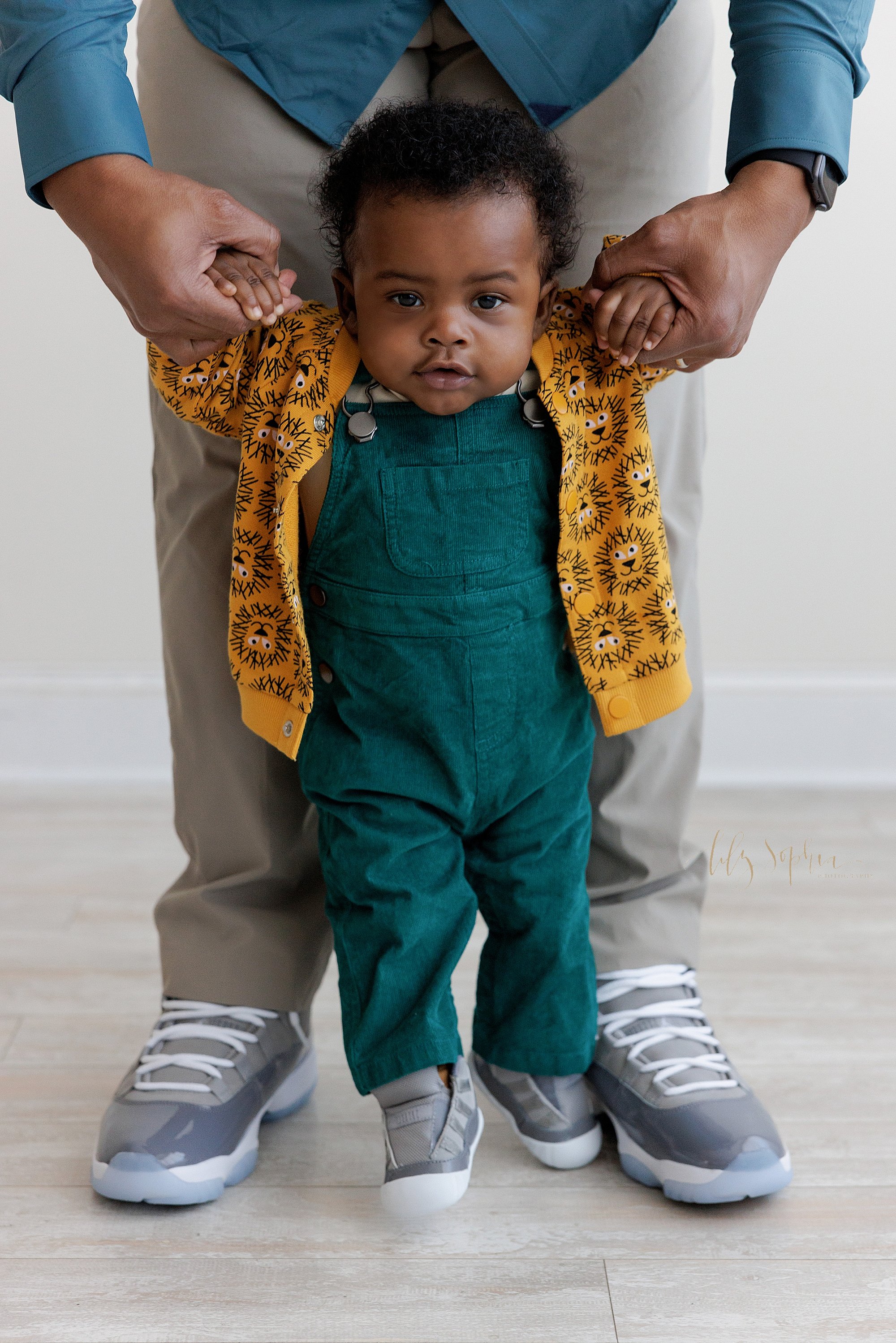  Baby photo of an African-American baby boy as he holds onto his father’s hands to try to walk in front of his father taken near Midtown in Atlanta in a photography studio that uses natural light. 