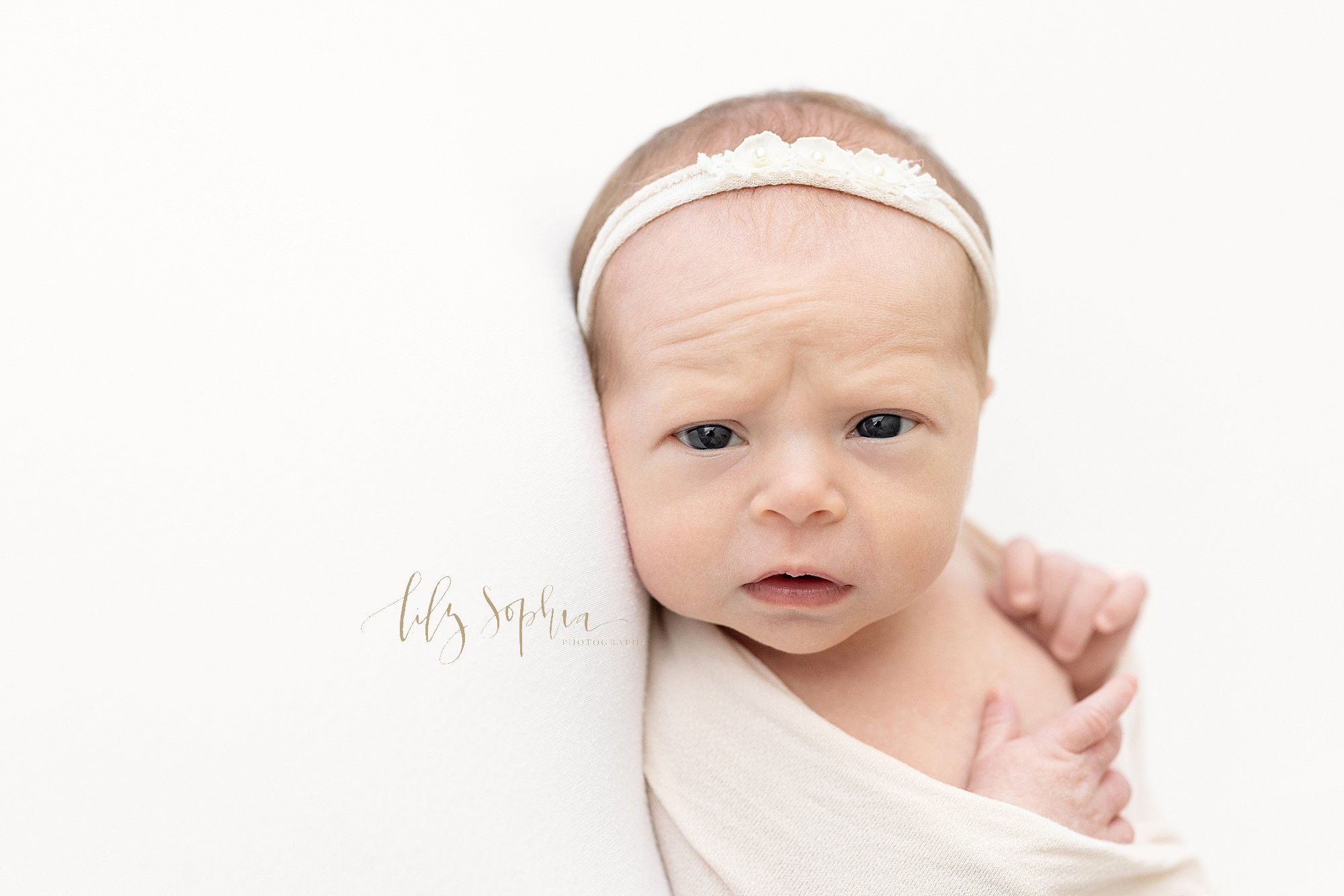  Newborn portrait of a wide awake newborn baby girl wearing a stretchy headband in her hair as she wonders where she is taken in a photography studio near Sandy Springs in Atlanta that uses natural light. 