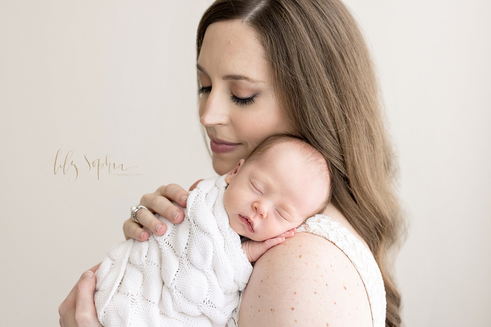  Newborn portrait of a mother holding her peacefully sleeping newborn baby girl on her shoulder as mom treasures these moments with her taken near Kirkwood in Atlanta in a photography studio that uses natural light. 