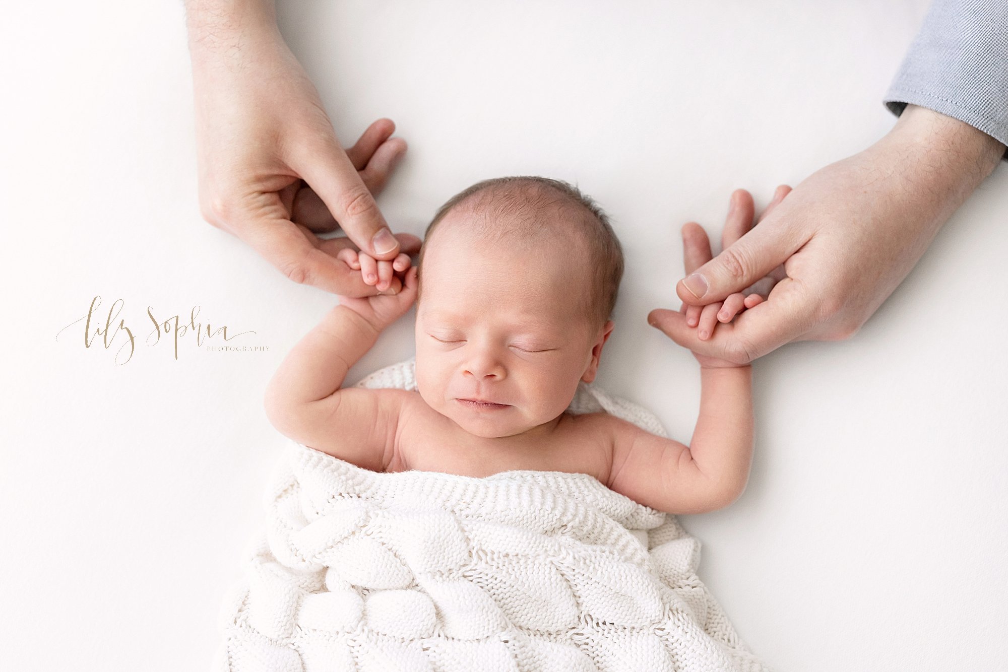  Newborn portrait with a newborn baby girl lying on her back and holding the pointer fingers of her father in her hands as she sleeps taken near Roswell in Atlanta in a natural light photography studio. 