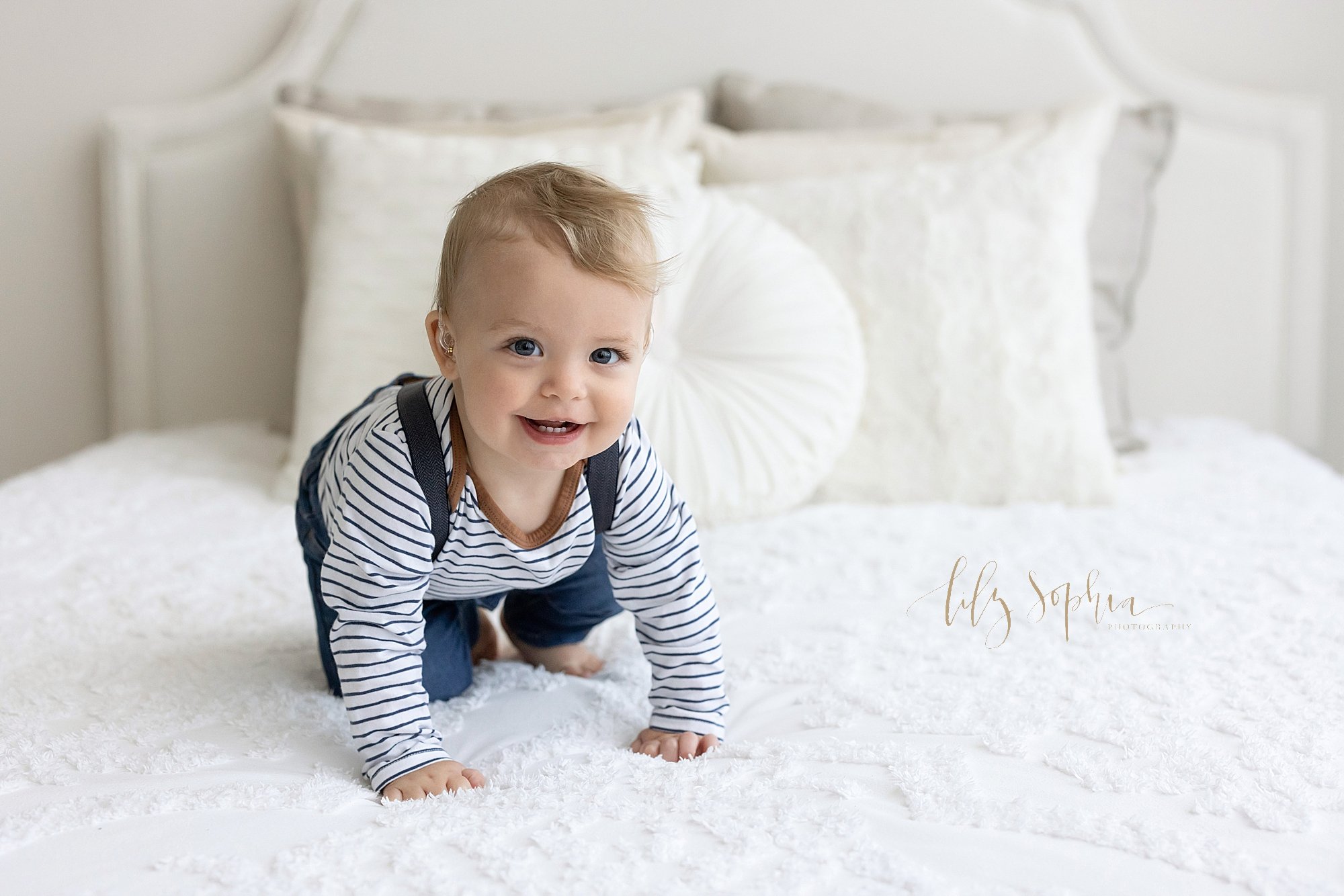  First birthday photo session with a one year old little boy as he crawls across a bed in a natural light studio near Kirkwood in Atlanta, Georgia. 