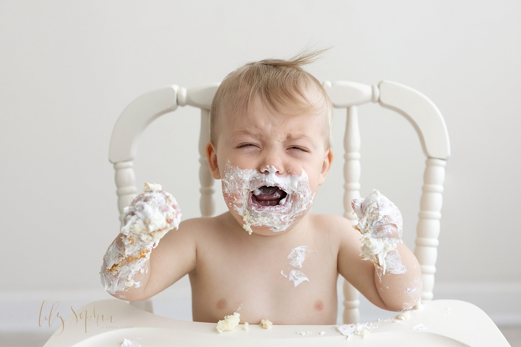 First birthday smash cake photo session of a one year old baby boy covered in icing and crying because his cake is taken away shot near Midtown in Atlanta in a natural light studio. 