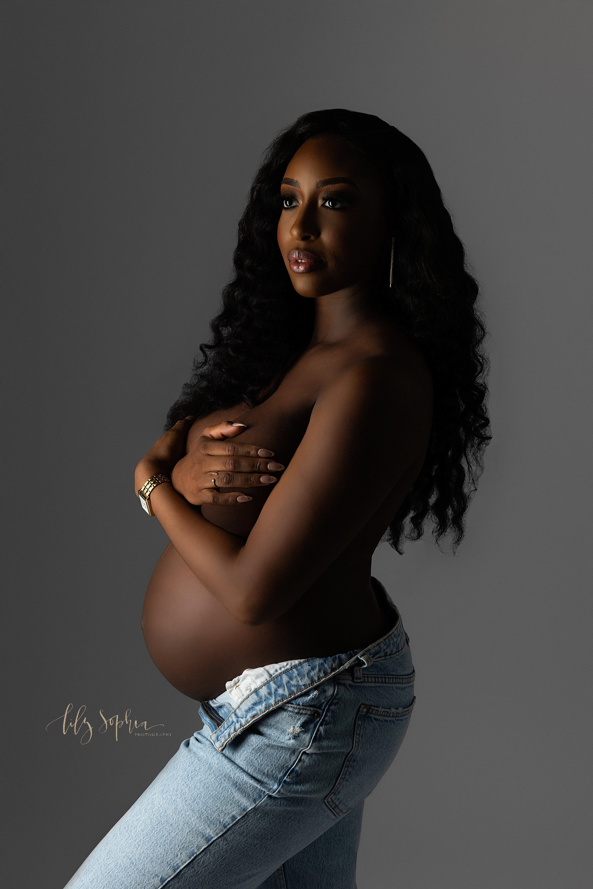  Modern maternity photo session with an African-American woman as she wears a pair of unzipped blue jeans taken near Morningside in Atlanta in a photography studio. 