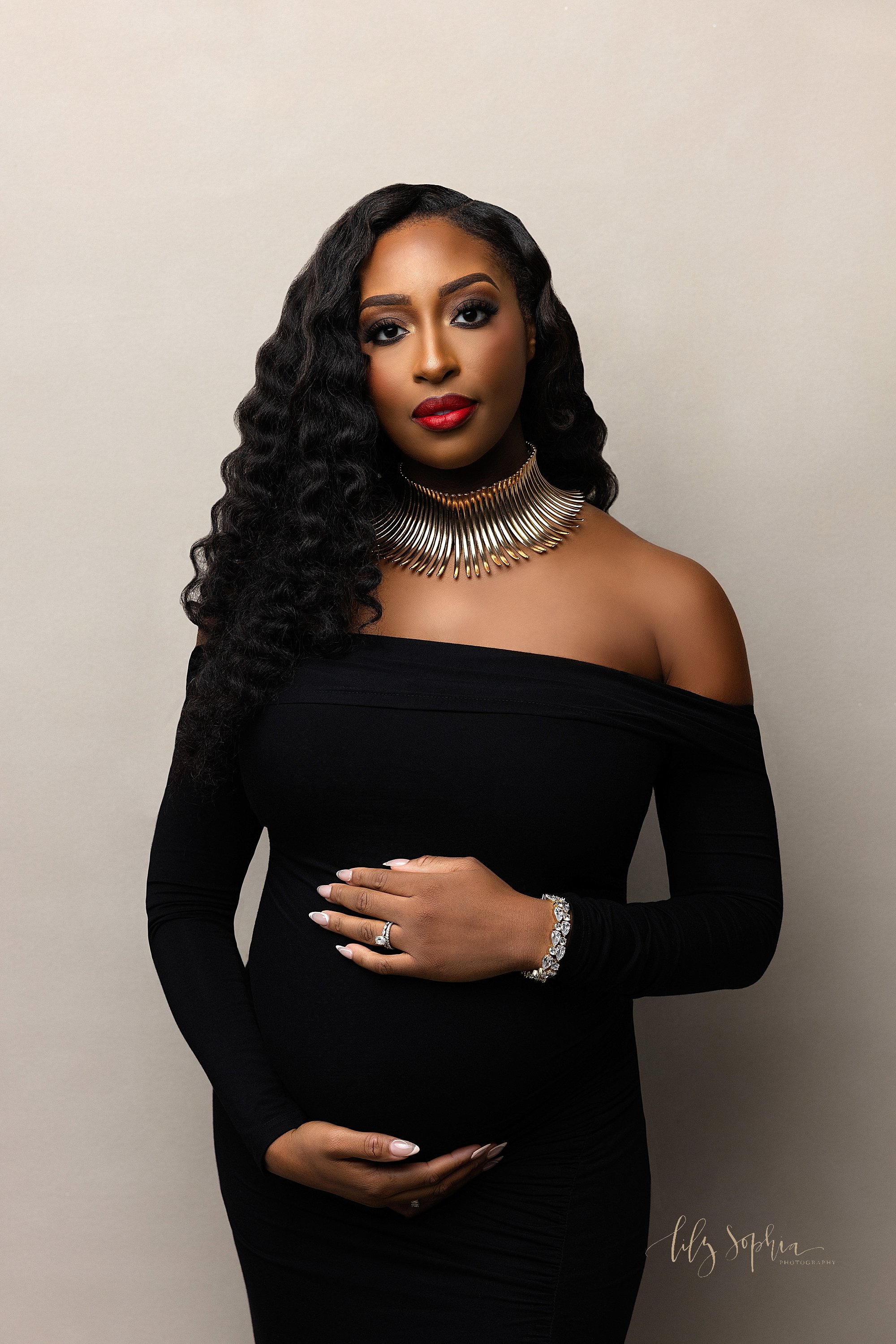  Modern maternity photo session with an African-American expectant mother wearing a black jersey knit long sleeve gown as she frames her belly with her hands taken in Ponce City Market in Atlanta at Lily Sophia Photography studio that uses natural li