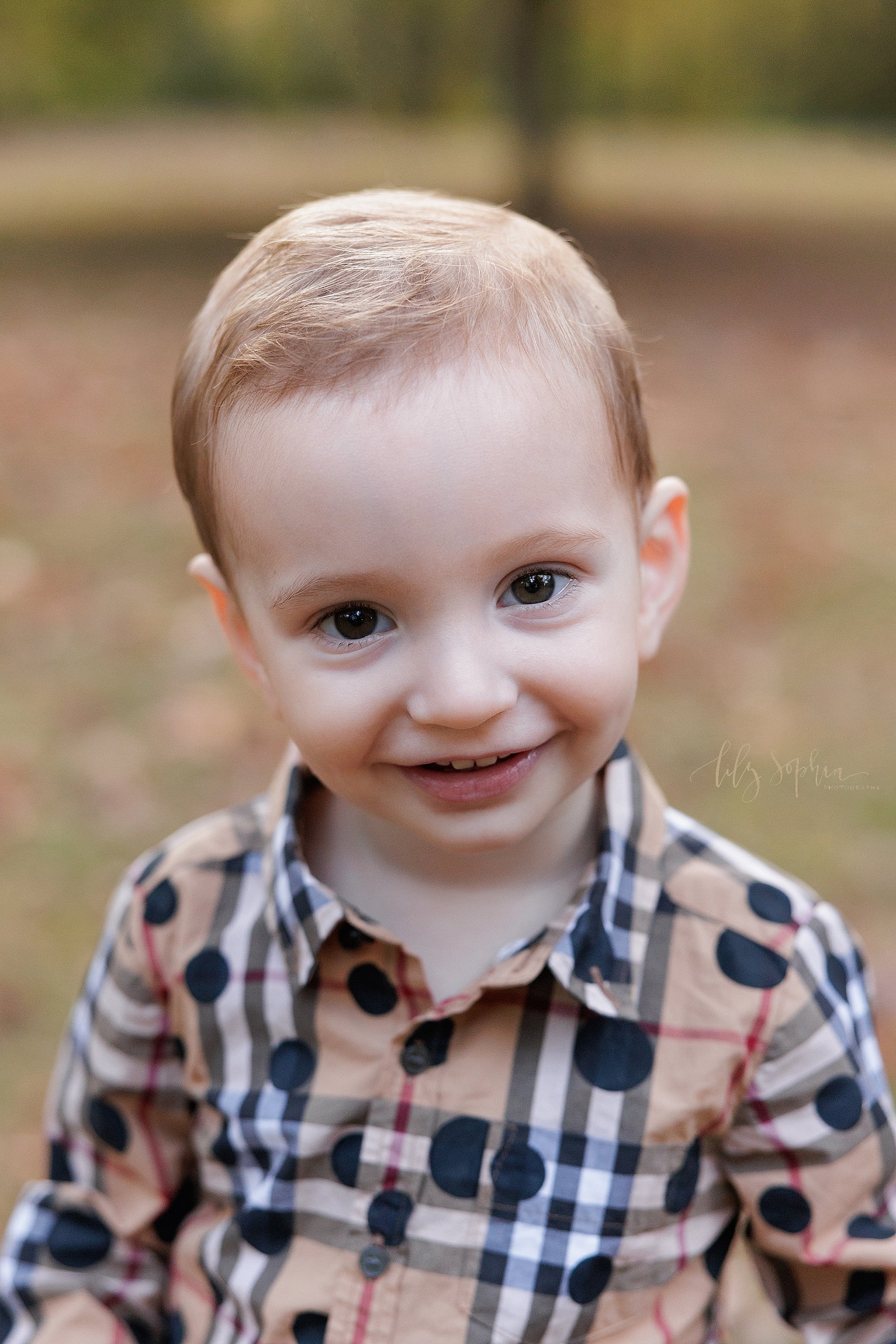  Close-up family photo of a toddler boy as he stands and smiles during autumn at sunset in an Atlanta park. 