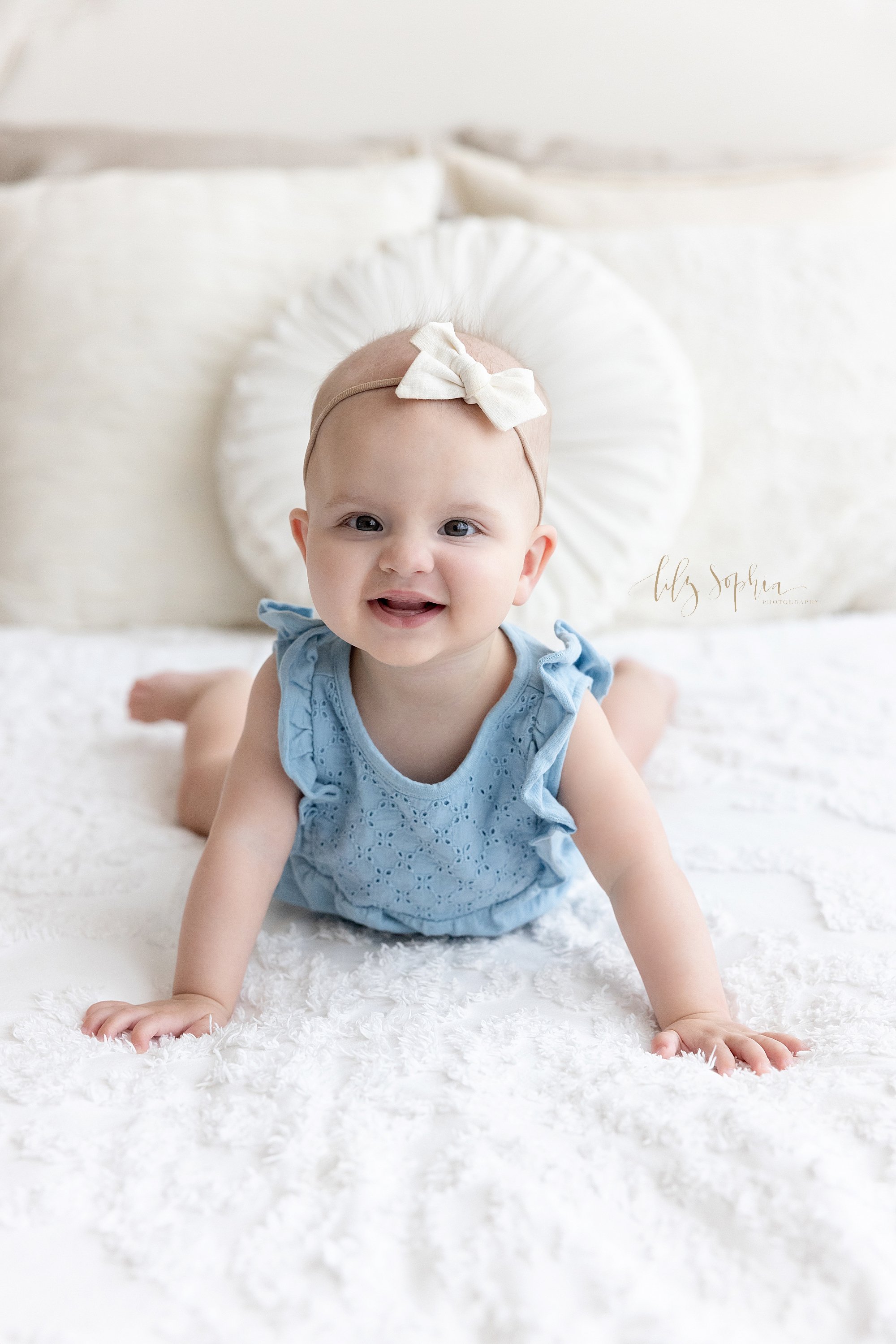  Baby portrait of a baby girl as she lies on her stomach on a bed and pushes herself up taken using natural light in a photography studio near Sandy Springs in Atlanta. 