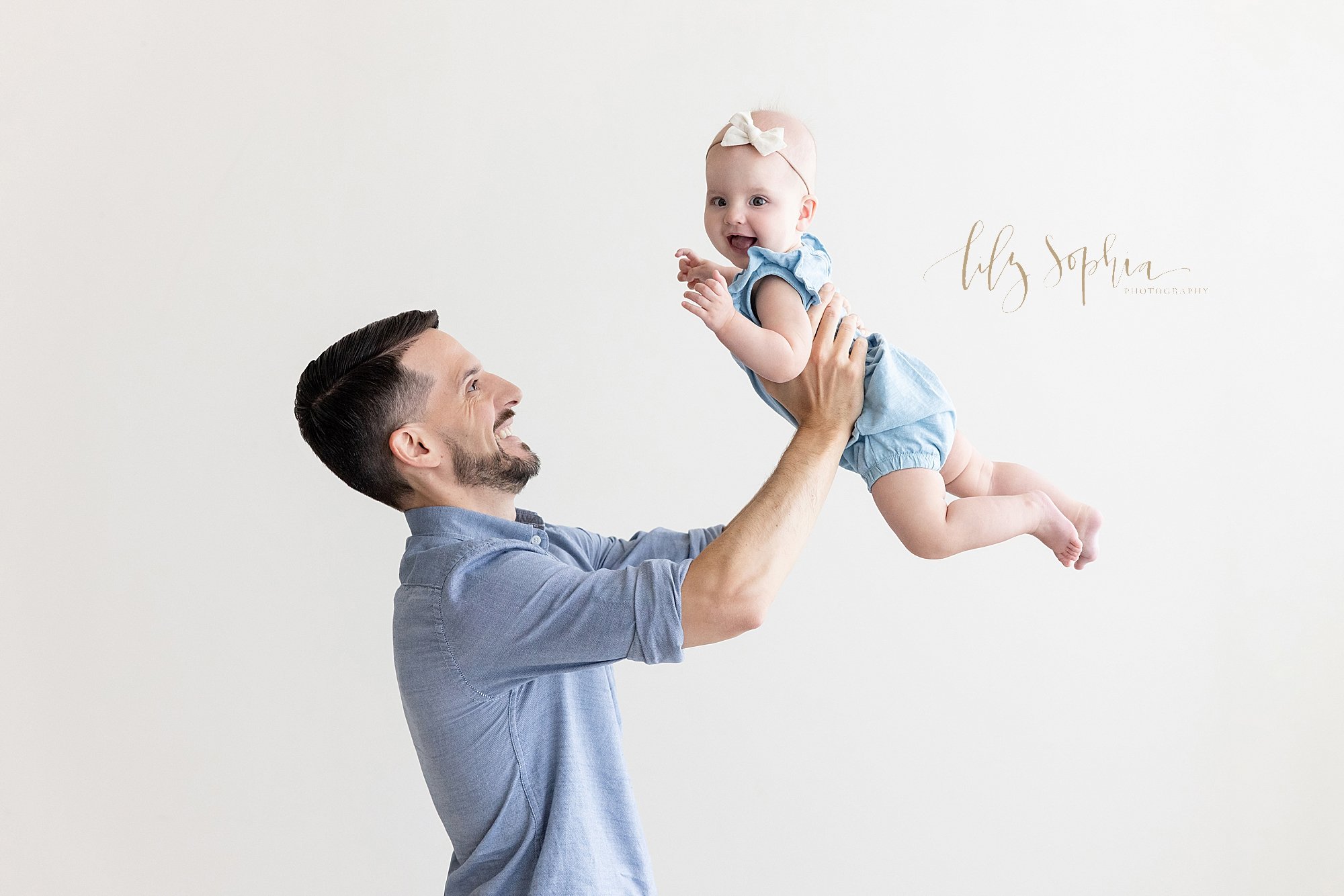  Family photo session with a father holding his baby girl above his head as she laughs taken in a studio that uses natural light near Atlanta in Midtown. 