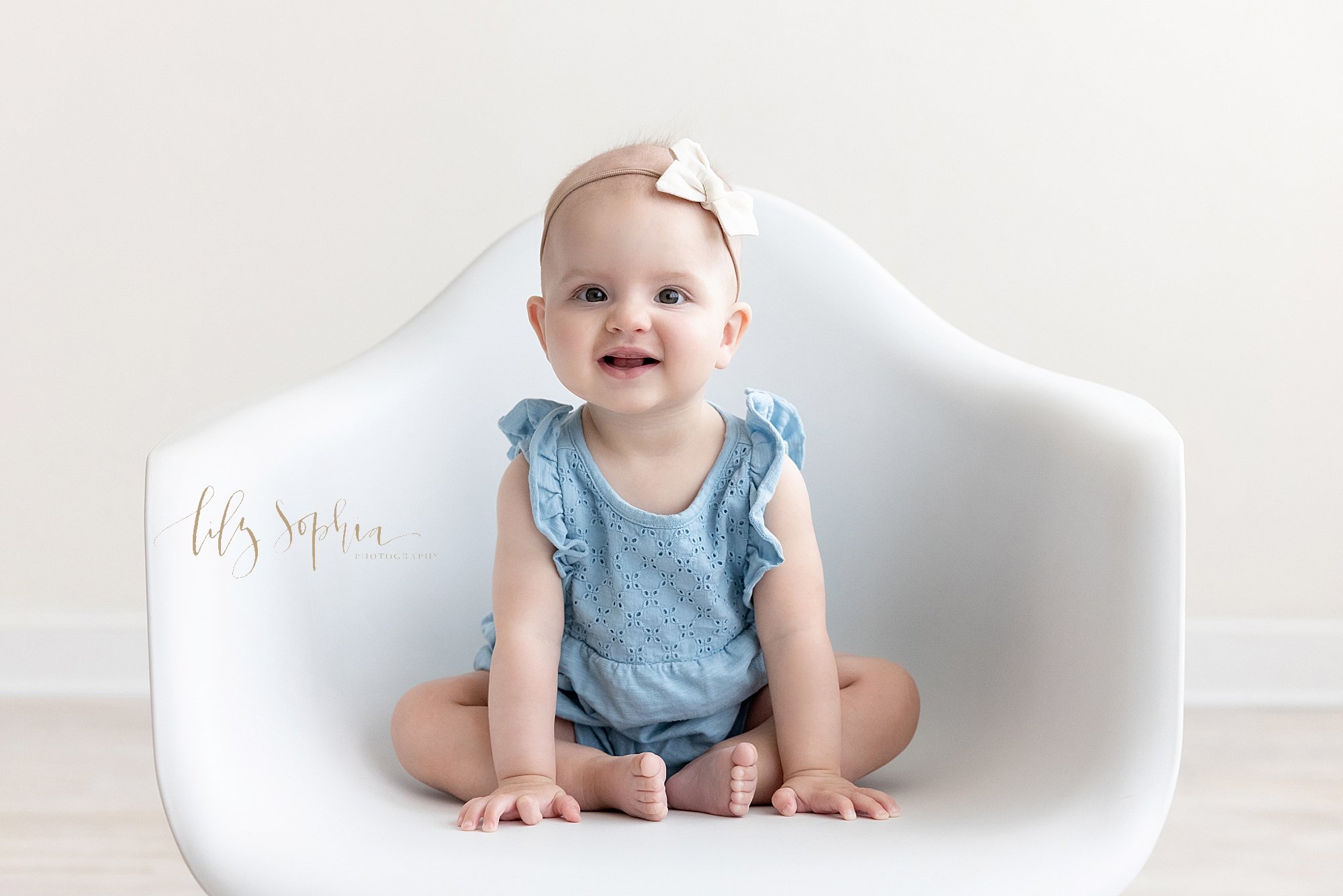  Sitting milestone photo session with a baby girl as she sits in a white molded chair in a natural light photography studio near Cumming in Atlanta, Georgia. 