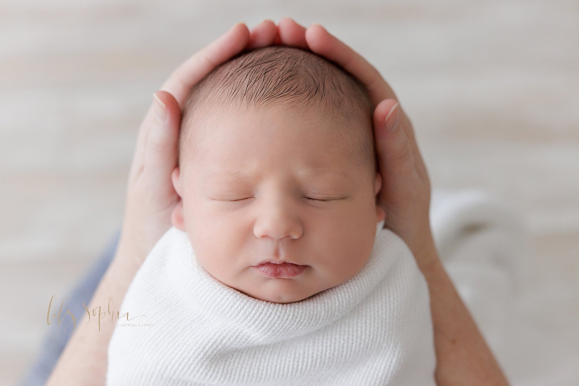  Newborn portrait of a newborn baby boy as his head is held in the hands of his mother taken in a photography studio that uses natural light near Kirkwood in Atlanta, Georgia. 
