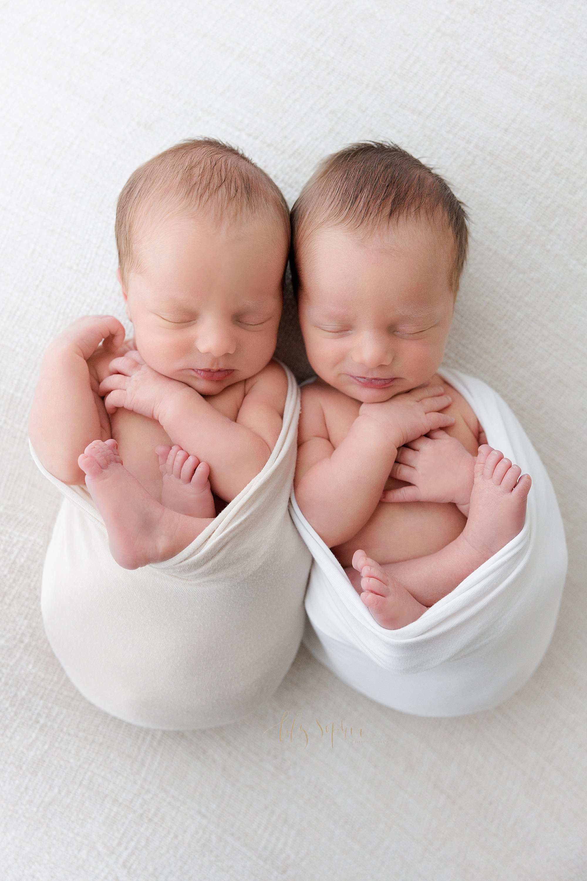  Newborn portrait of identical twin newborn baby boys as they lie side by side cradled in stretchy swaddles in a photography studio near Cumming in Atlanta Georgia that uses natural light. 