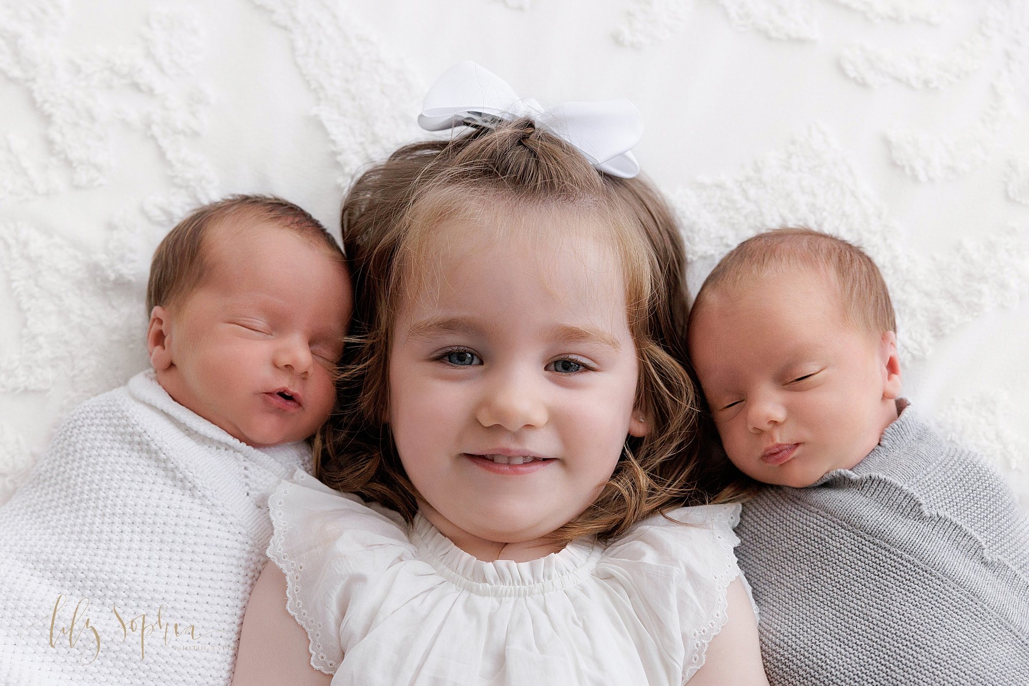  Family newborn portrait of newborn identical twin boys as they lie on their backs with their older sister between them taken near Buckhead in Atlanta in a photography studio that uses natural light. 