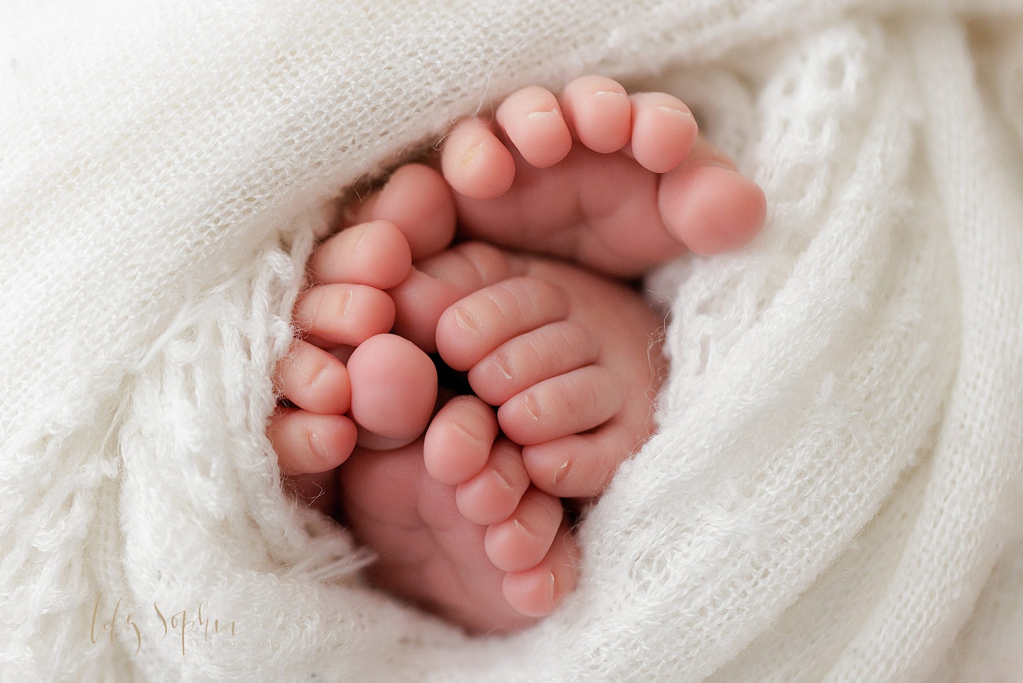  The four feet of newborn baby identical twins peek out from a soft white blanket taken near Kirkwood in Atlanta in a natural light photography studio. 