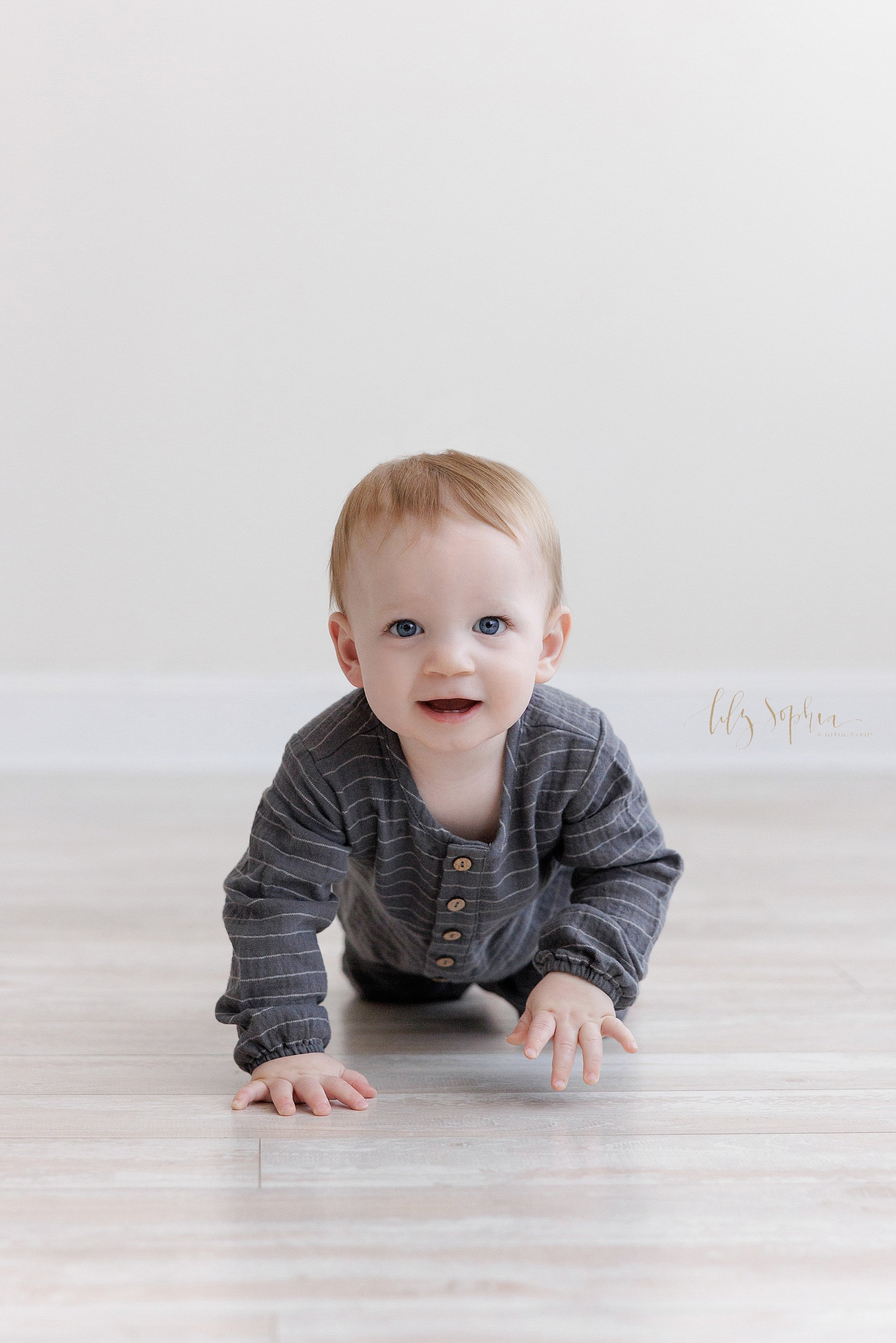  First birthday picture of a one year old baby boy as he crawls across the floor in a photography studio near Roswell in Atlanta that uses natural light. 