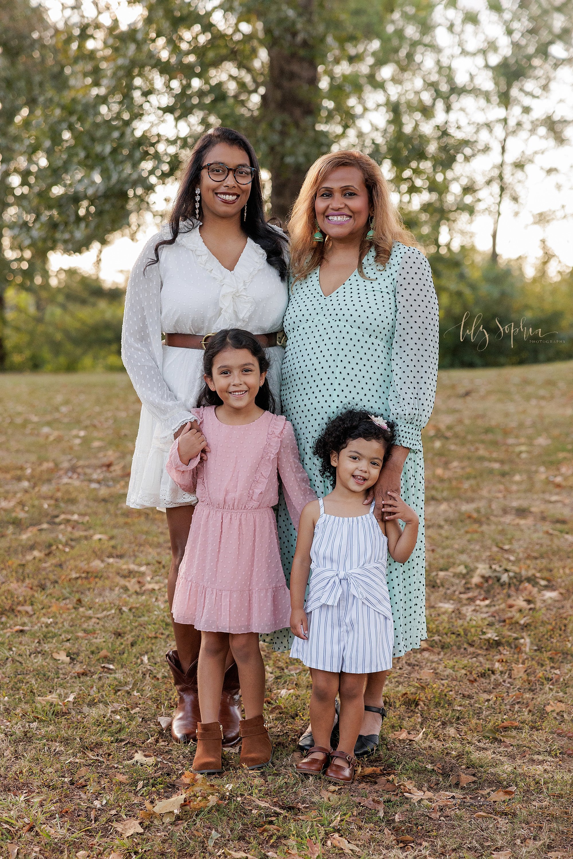  Multi-generational family photo of a grandmother, her daughter, and her two granddaughters taken during autumn at sunset in an Atlanta park. 