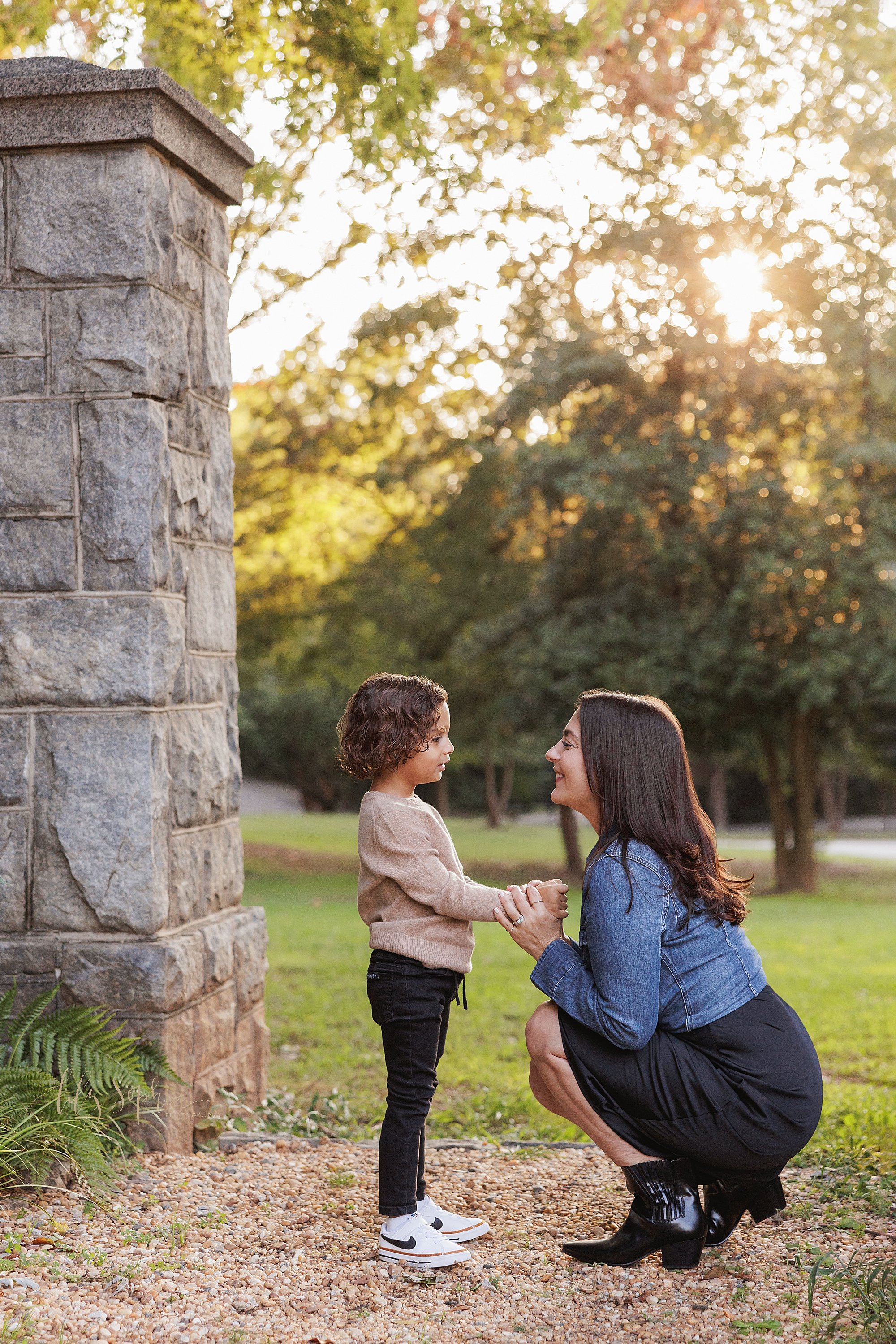  Family mother and son portrait as they talk with one another between a stone entranceway in an Atlanta park at sunset. 