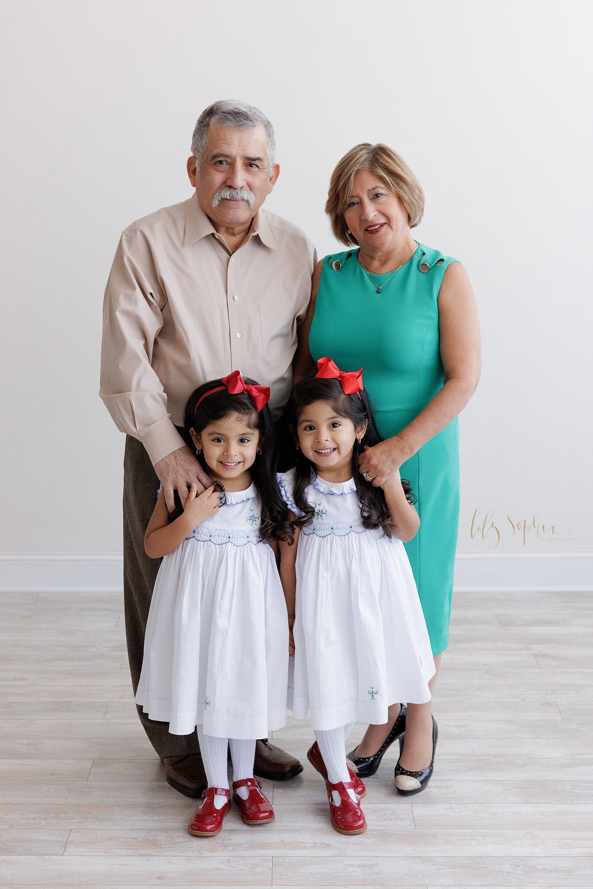  Family photo session with grandparents standing behind their granddaughters and holding their hands taken near Alpharetta in Atlanta in a natural light photography studio. 