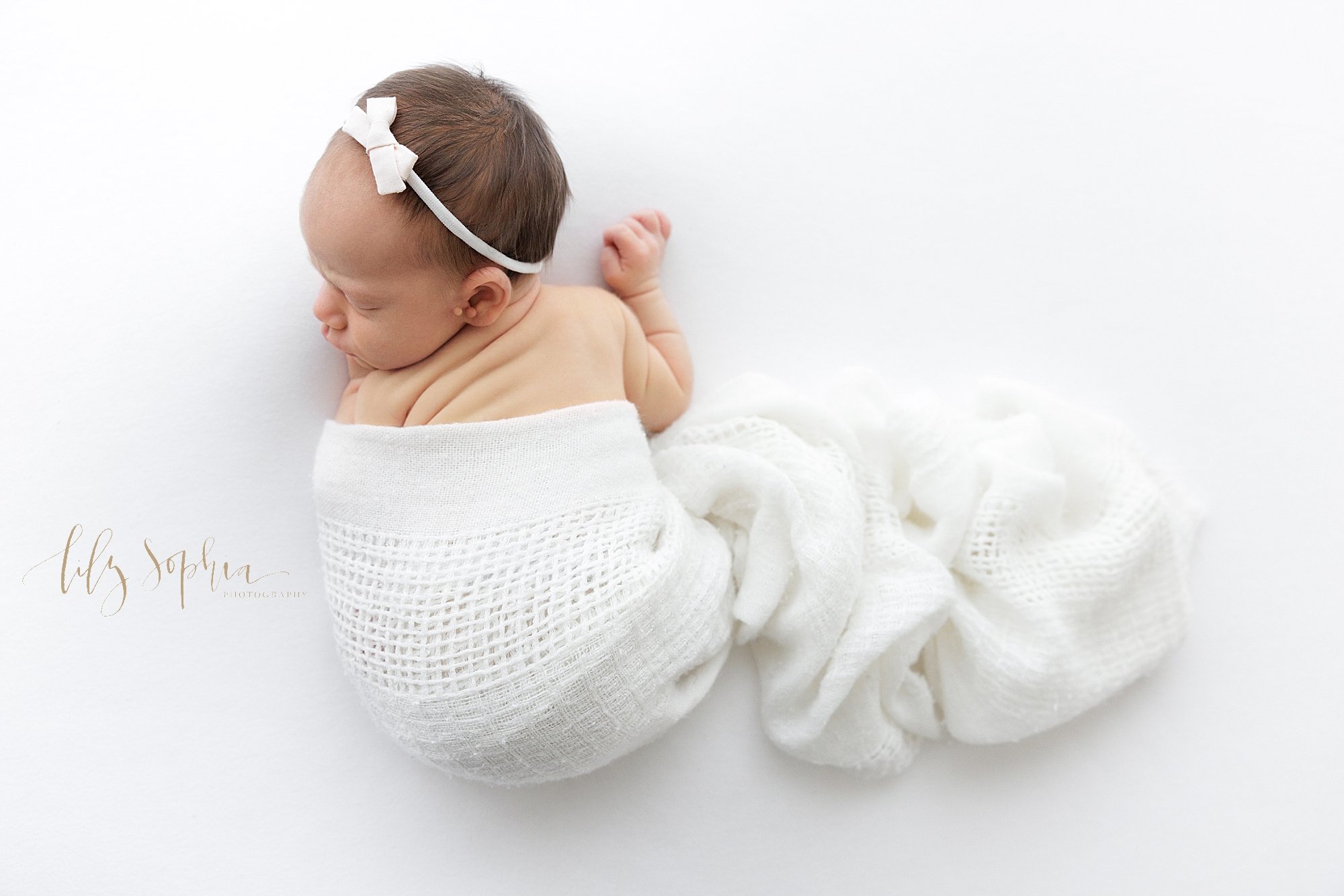  Newborn portrait of a newborn baby girl lying on her stomach as she turns her head over her left shoulder and the rolls on her back can be seen taken using natural light in a photography studio near Vinings in Atlanta. 