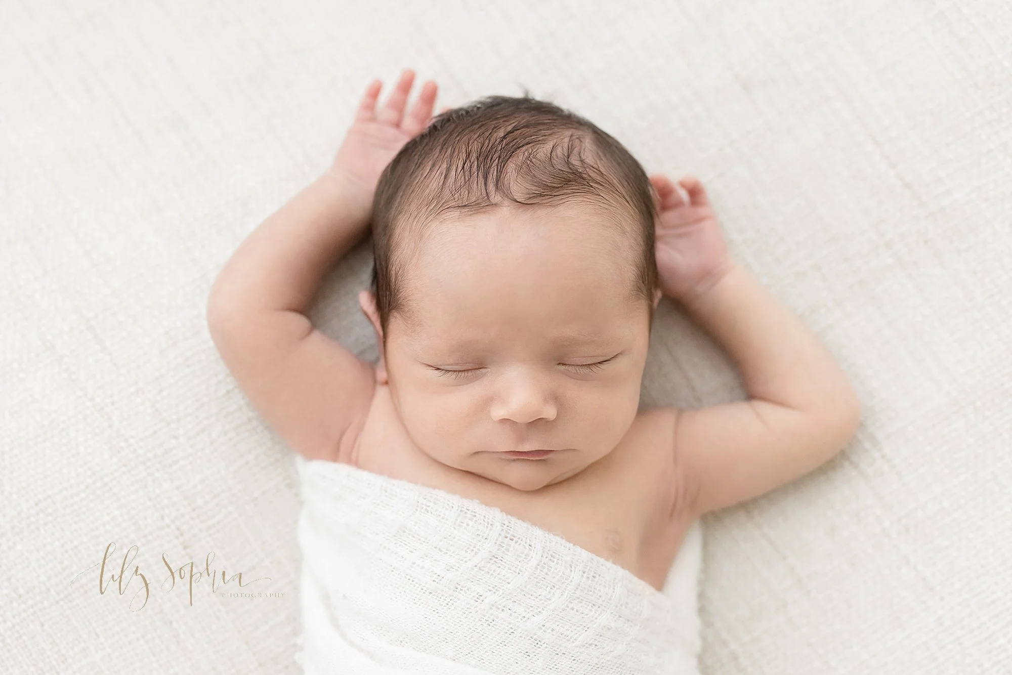  Newborn portrait of a peacefully sleeping baby boy lying on his back with his hands raised above his head taken in a natural light photography studio near Sandy Springs in Atlanta. 