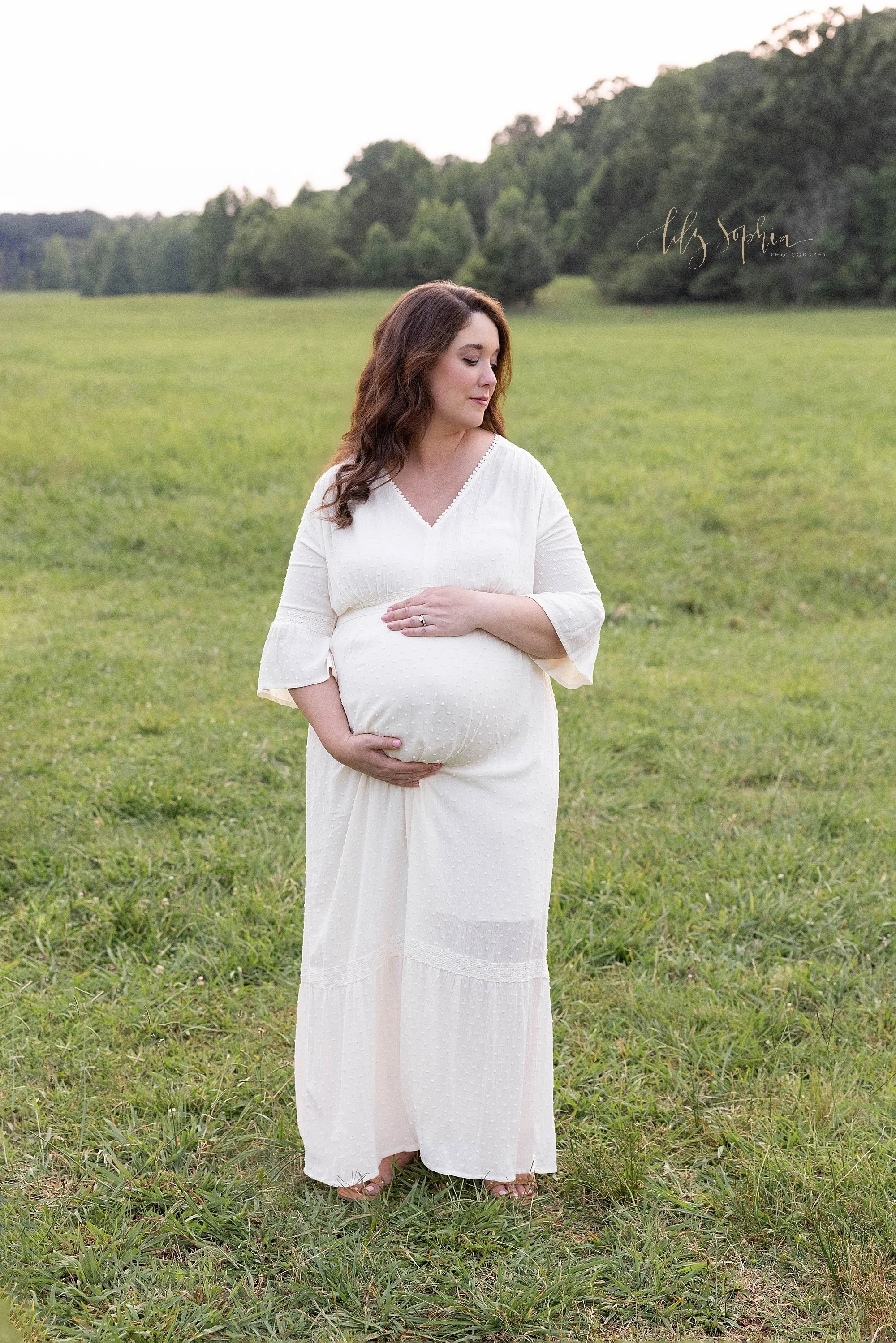  Maternity photo session in a field near Atlanta, Georgia as she stands framing her womb with her hands and looking over her left shoulder at sunset. 