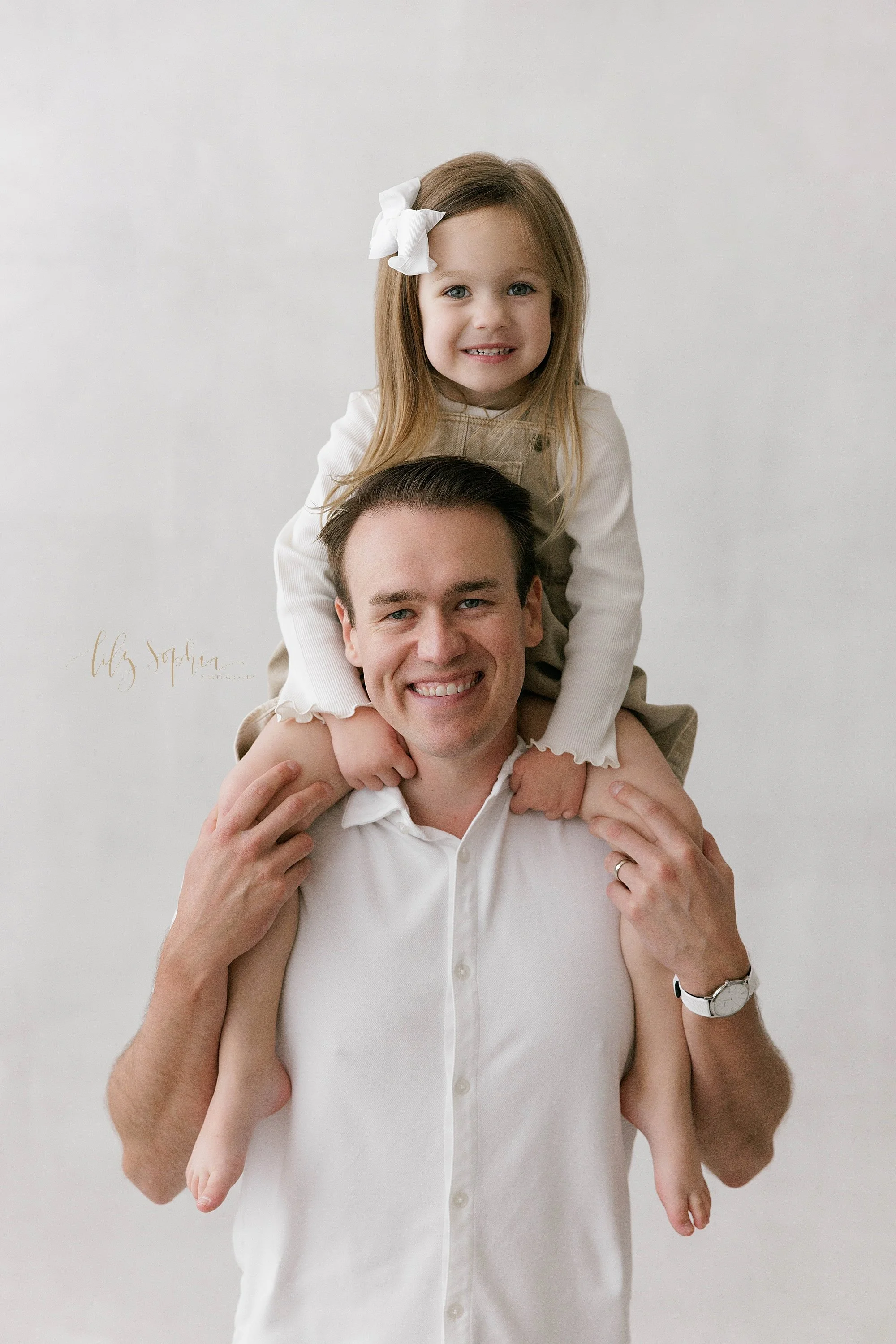  A father and daughter photo with the young girl riding on her dad’s shoulders taken in a natural light photography studio near Virginia Highlands in Atlanta. 