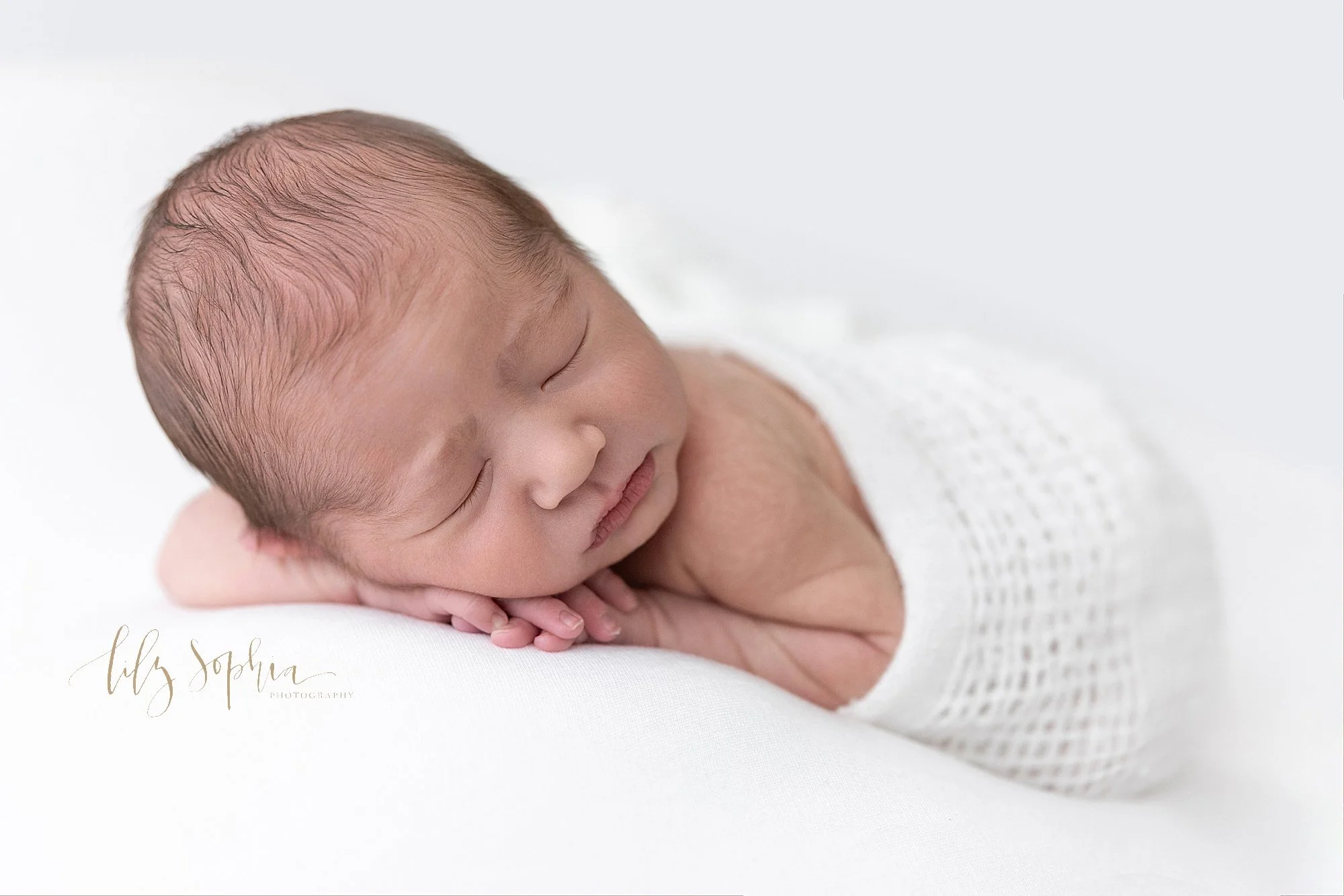  Newborn portrait of a sleeping newborn baby boy as he lays his head on top of his hands and he looks over his left shoulder taken near Midtown in Atlanta, Georgia in a photography studio that uses natural light. 