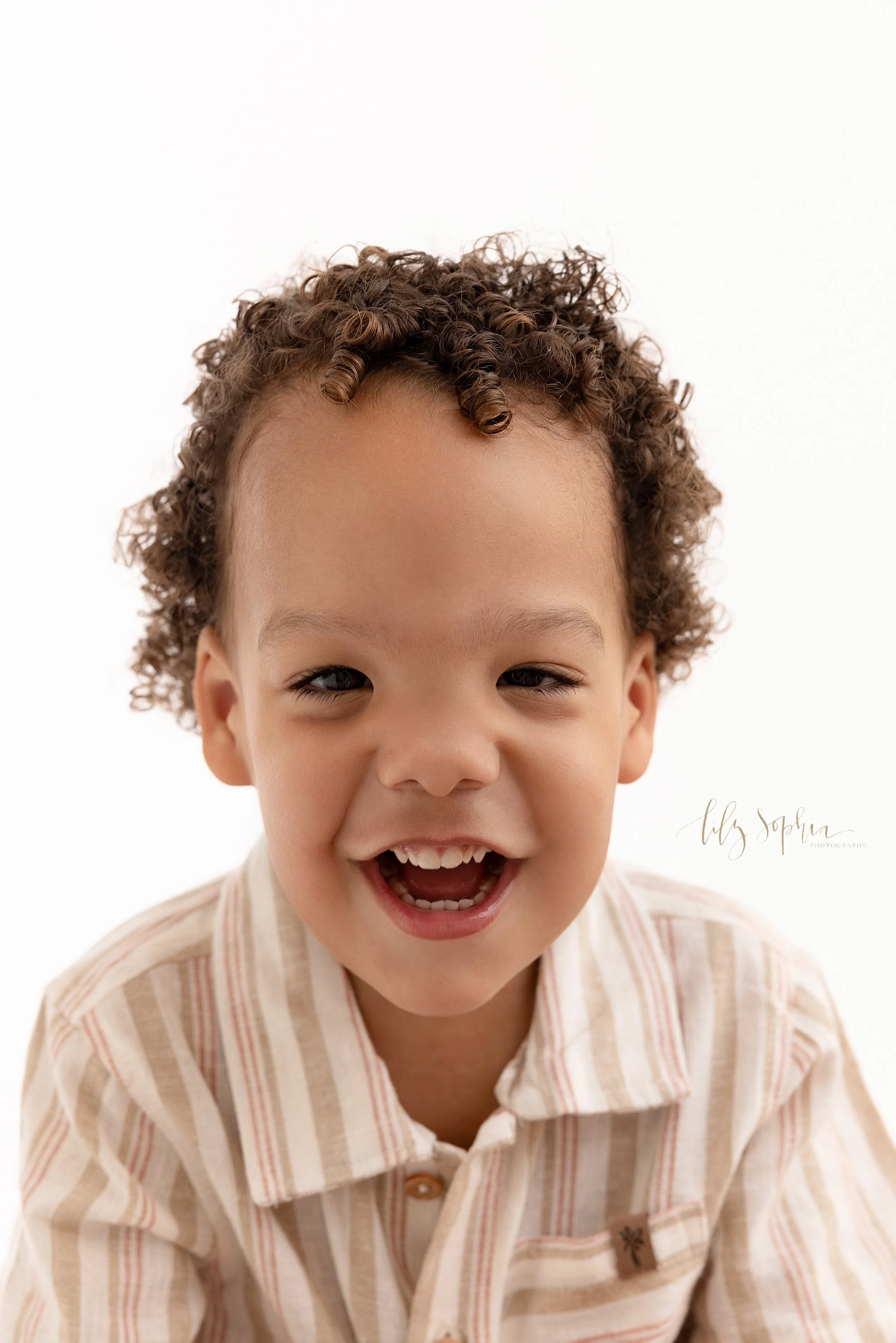  Close-up portrait of a happy toddler boy to remember the curly hair and all the tiny teeth taken near Kirkwood in Atlanta in natural light in a photography studio. 