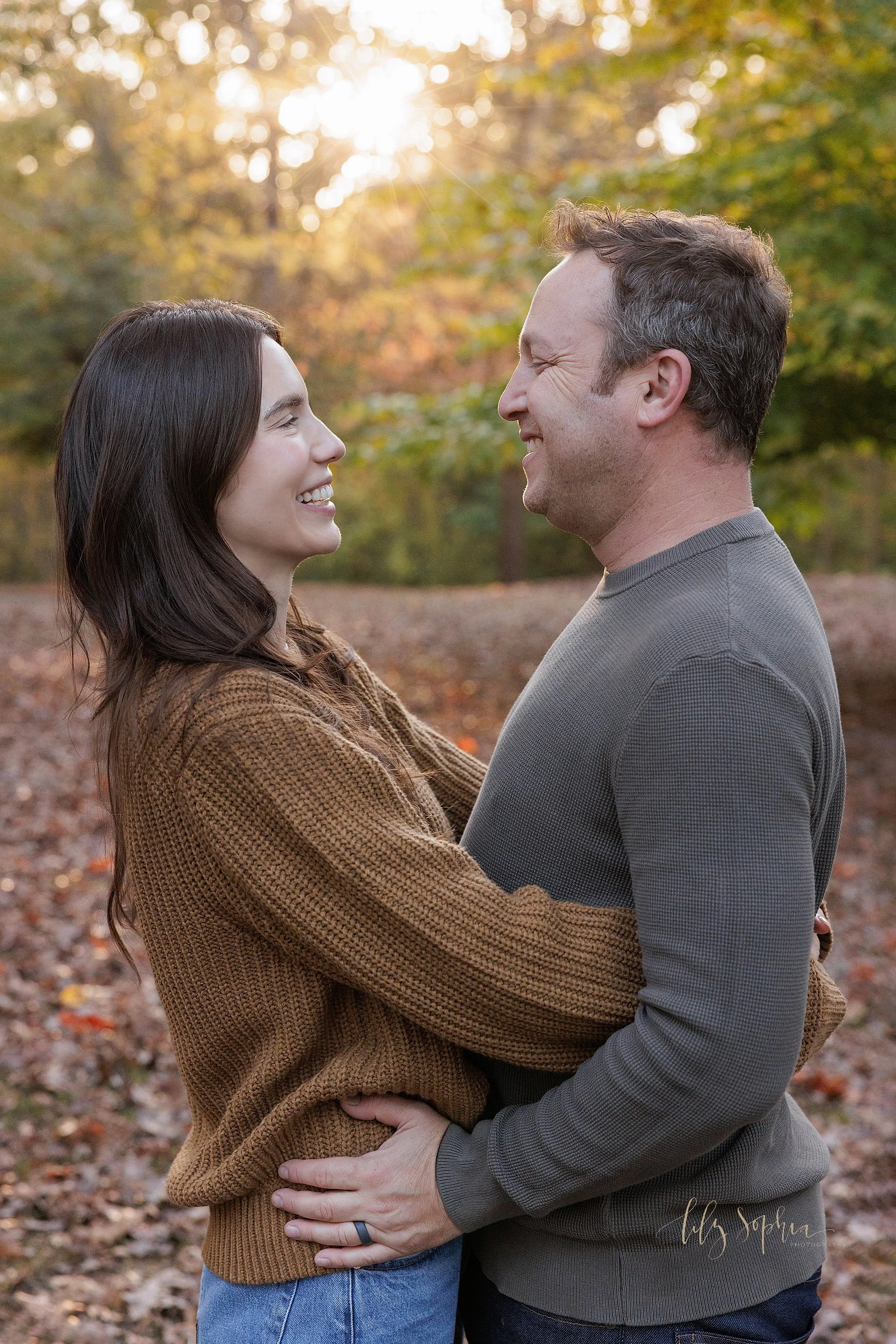  Family picture of a husband and wife as they stand and hold one another close to talk amongst the autumn leaves at sunset in a park near Atlanta, Georgia. 