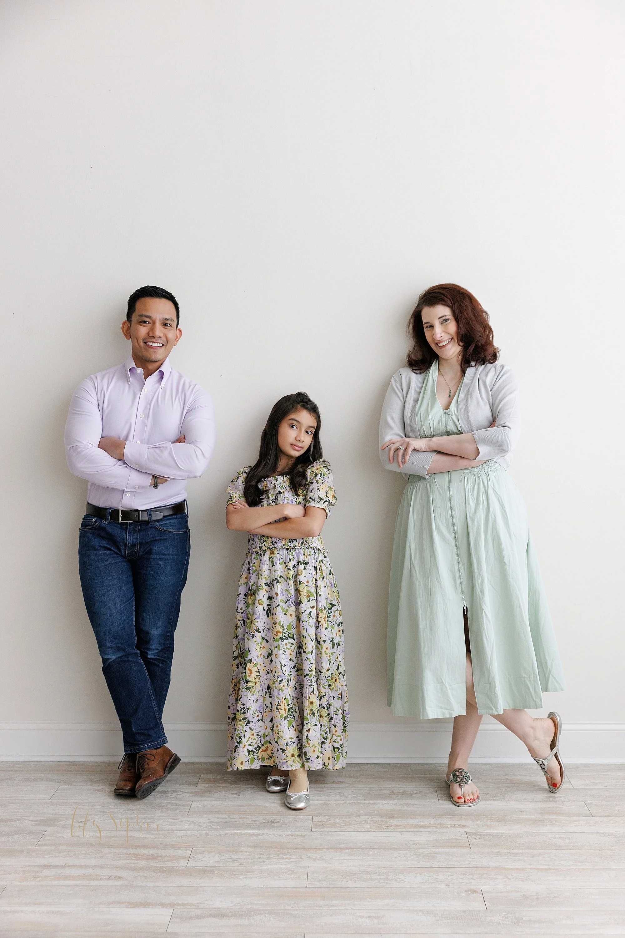  Family photography session as a daughter stands between her parents with all of them folding their hands in front of them taken in a natural light studio near Smyrna in Atlanta, Georgia. 